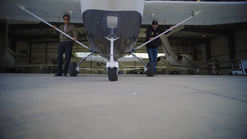 Two ground crew members moving a light aircraft into a hangar &mdash; Workers&rsquo; Compensation for Aviation Businesses article by Tricrest Insurance