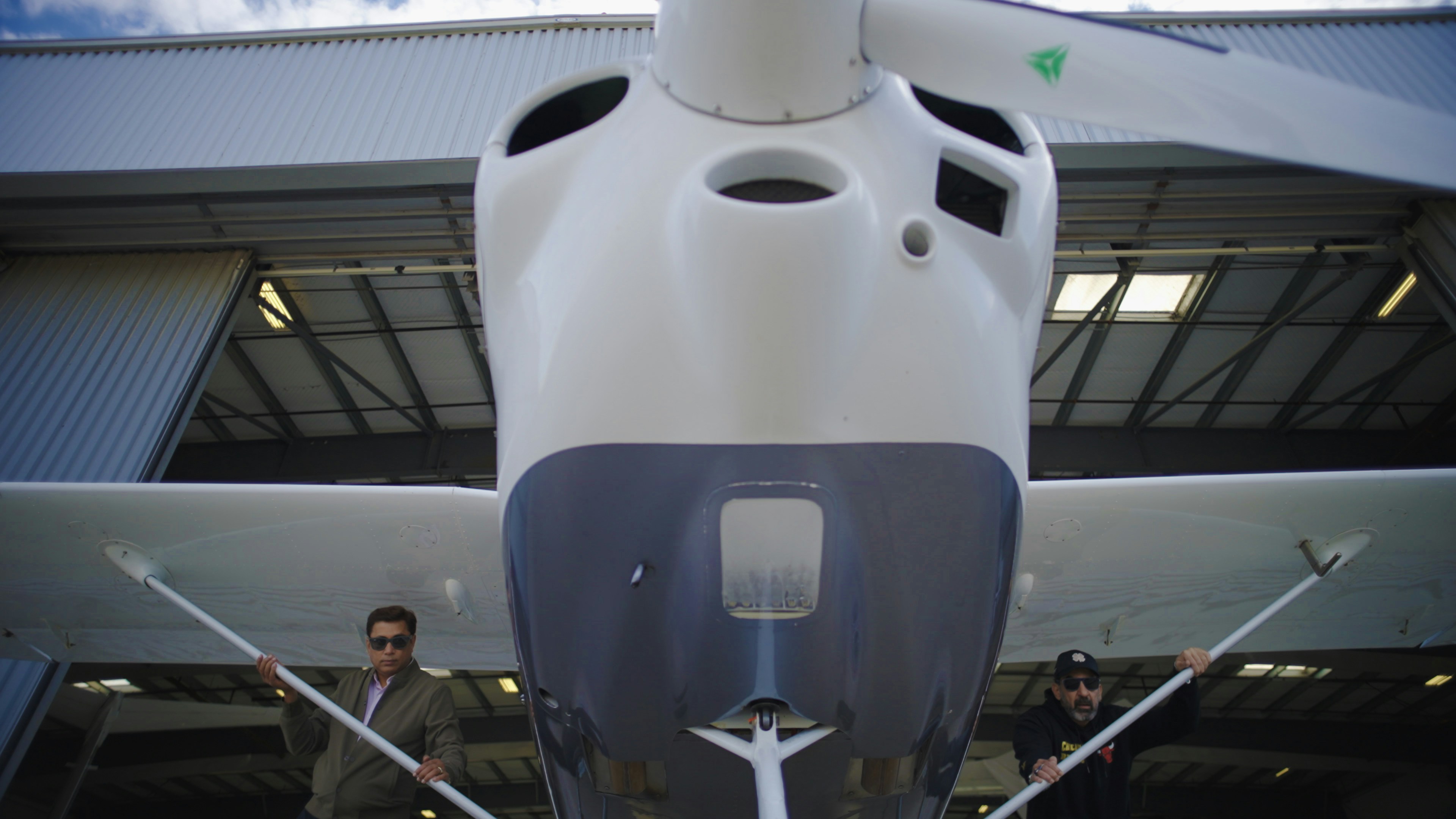 Two men stand by a small airplane in a hangar.