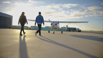 Two people walk towards a small airplane on tarmac.