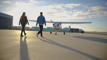 Two people walk towards a small airplane on tarmac.