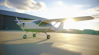 Small airplane parked on tarmac near hangar.