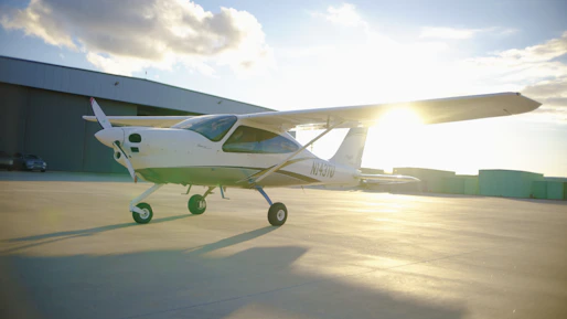 Small airplane parked on tarmac near hangar.