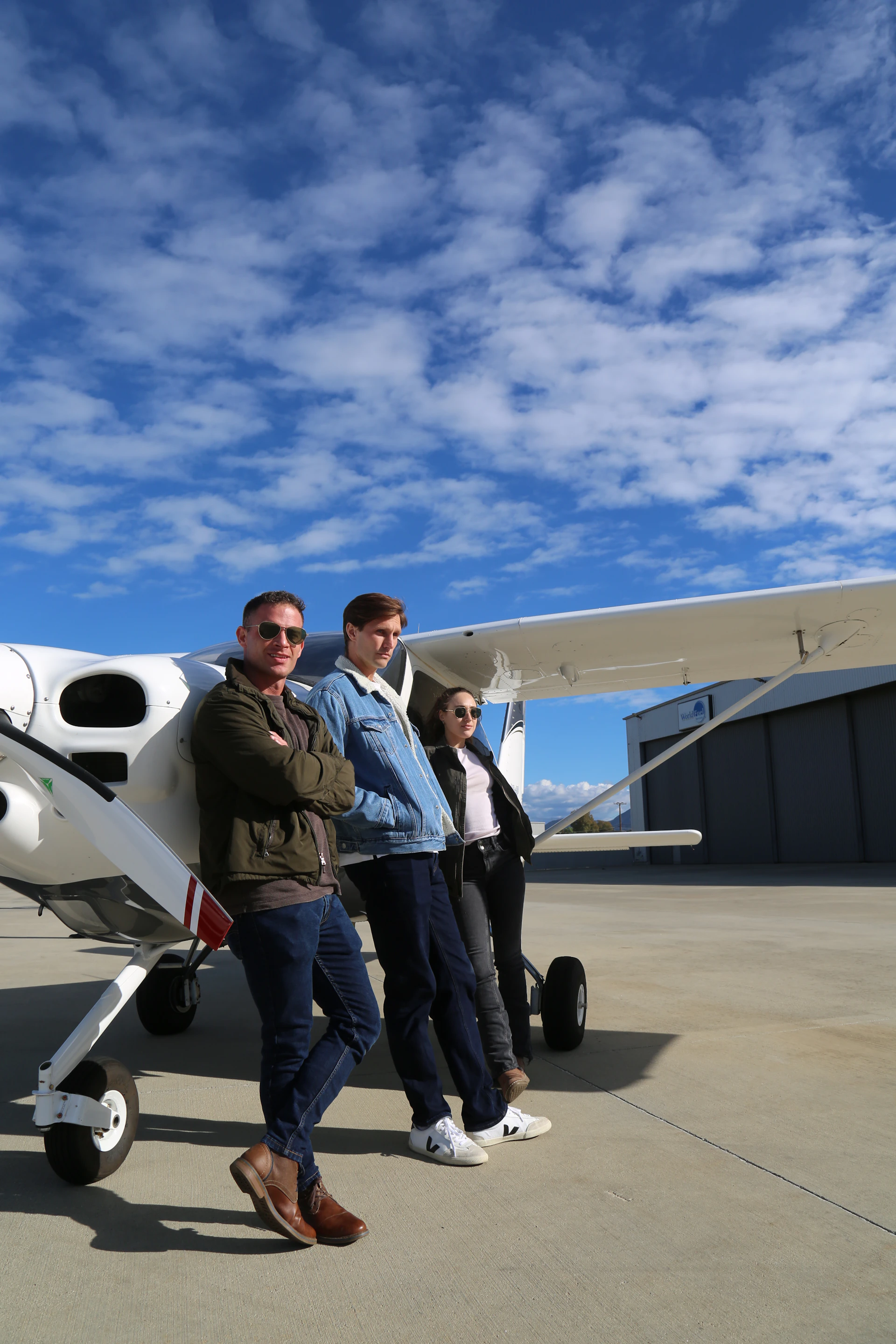 Three people stand by a small airplane outdoors.