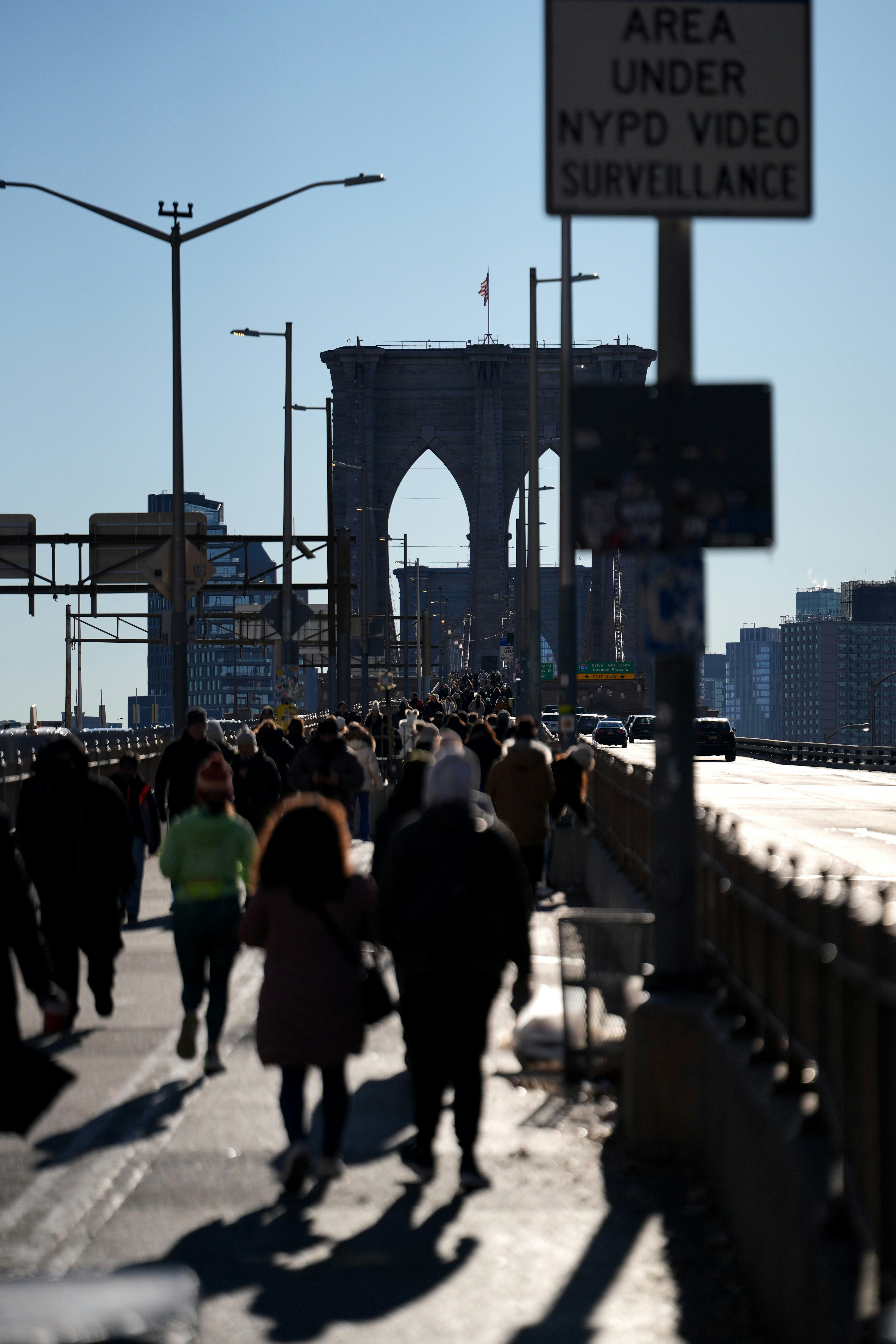 People walk across the brooklyn bridge on a sunny day.