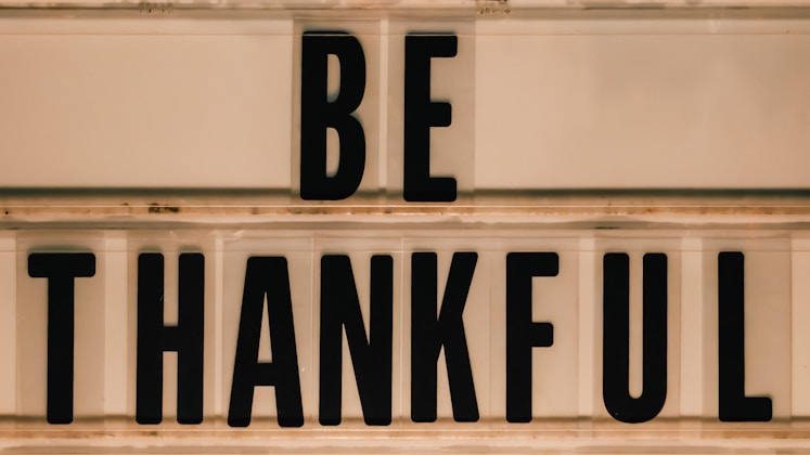 Black letters spell out "be thankful" on a sign.