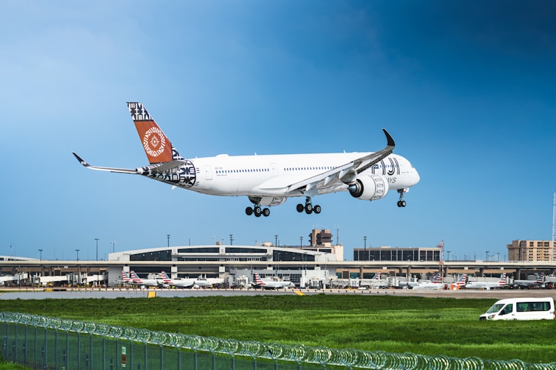 Airplane landing at the airport with buildings and grass.