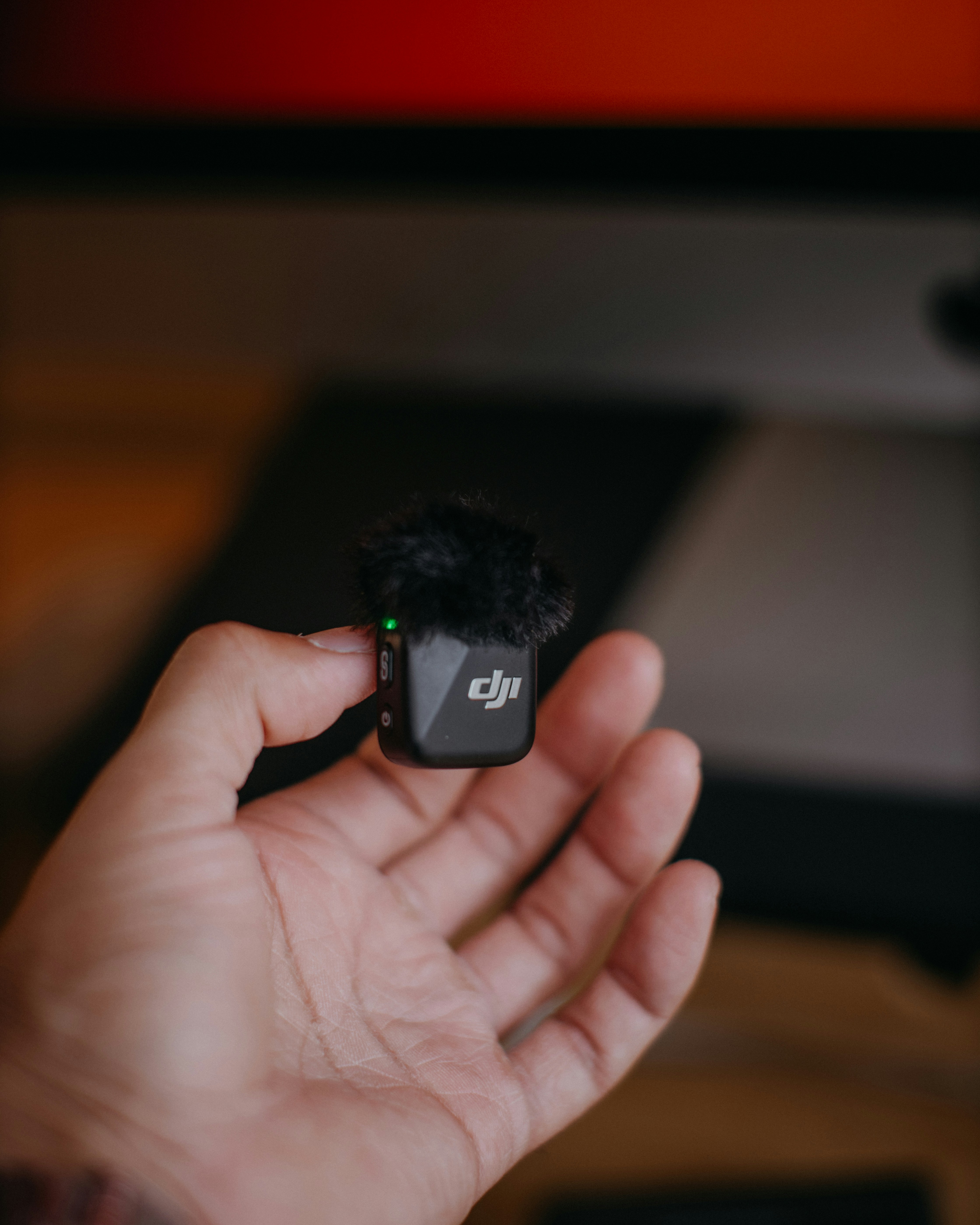 Hand holding a small black dji microphone with furry windscreen
