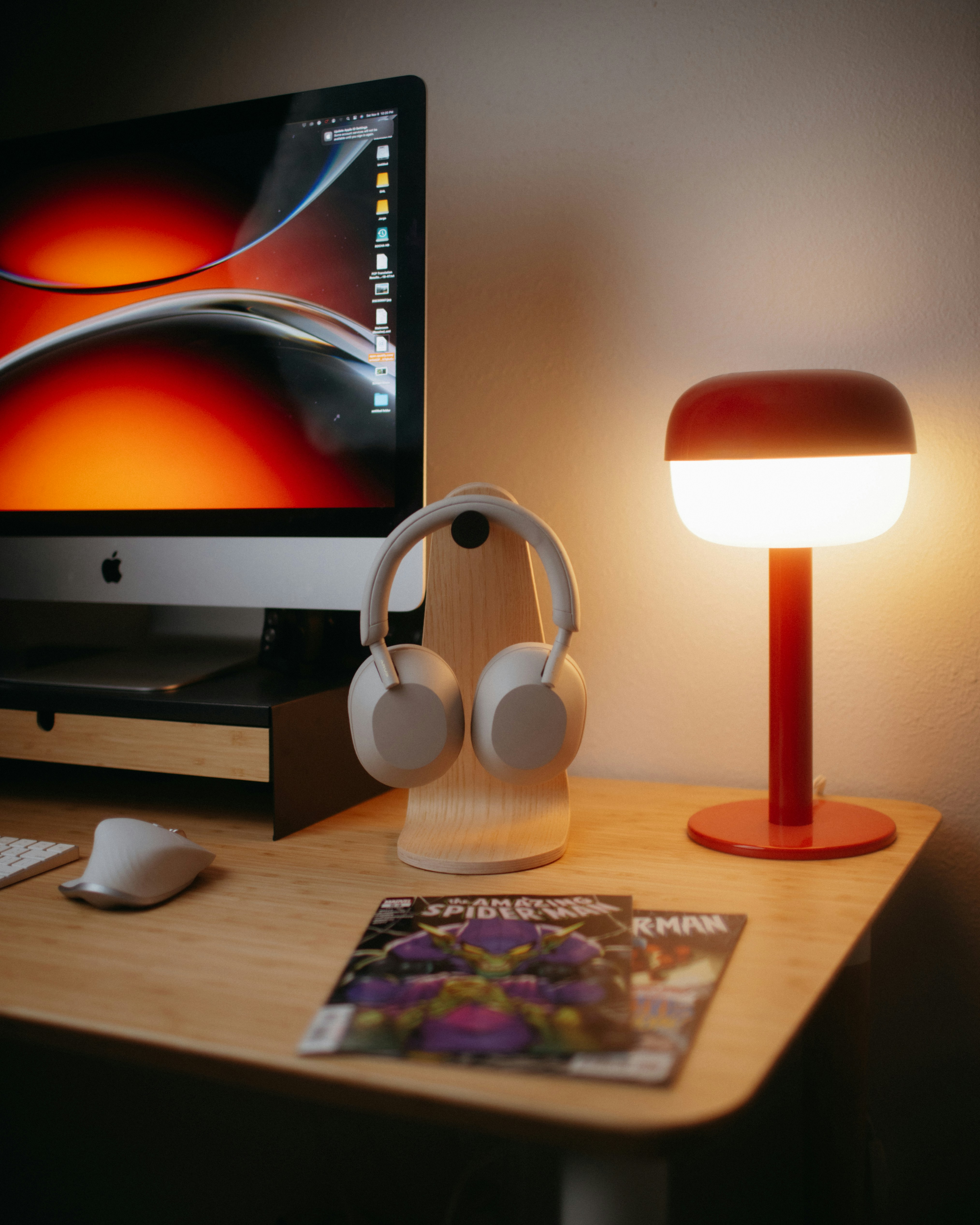 Desk with computer, headphones, lamp, and magazines.