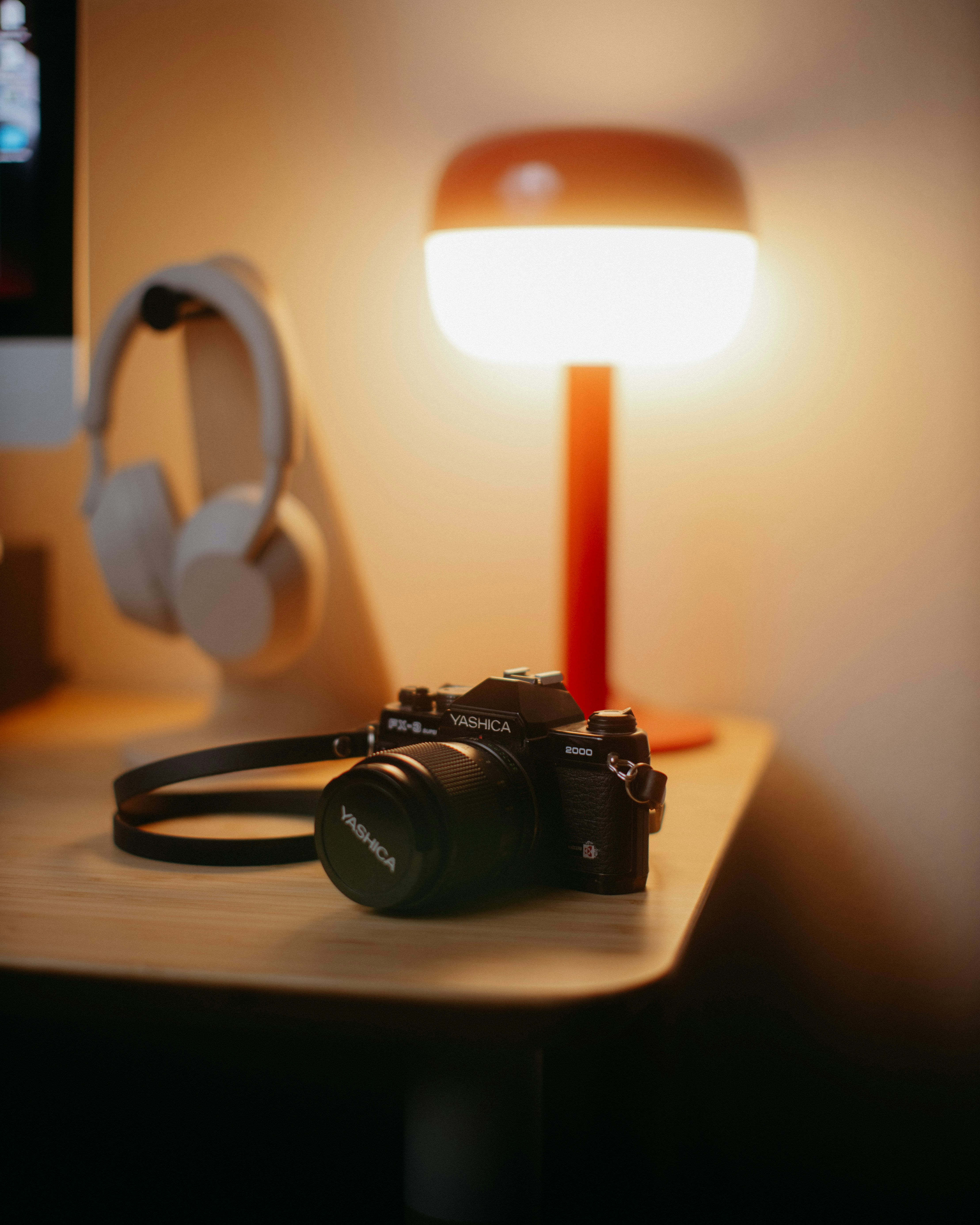 Camera and headphones on a desk with lamp