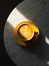 A yellow cup of coffee with latte art on table.