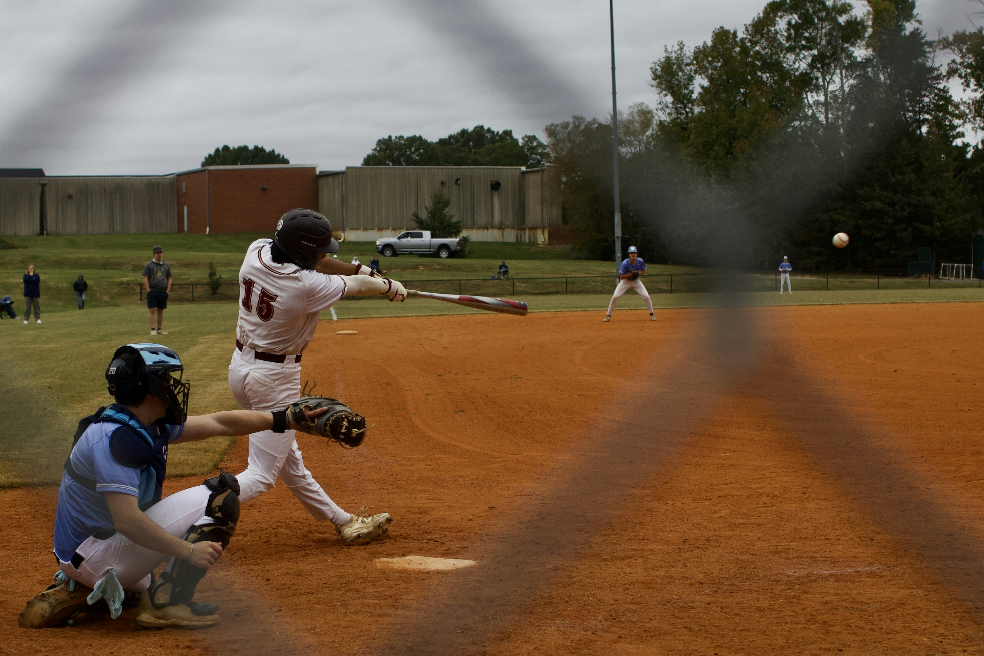 Baseball player swings bat at ball with catcher ready