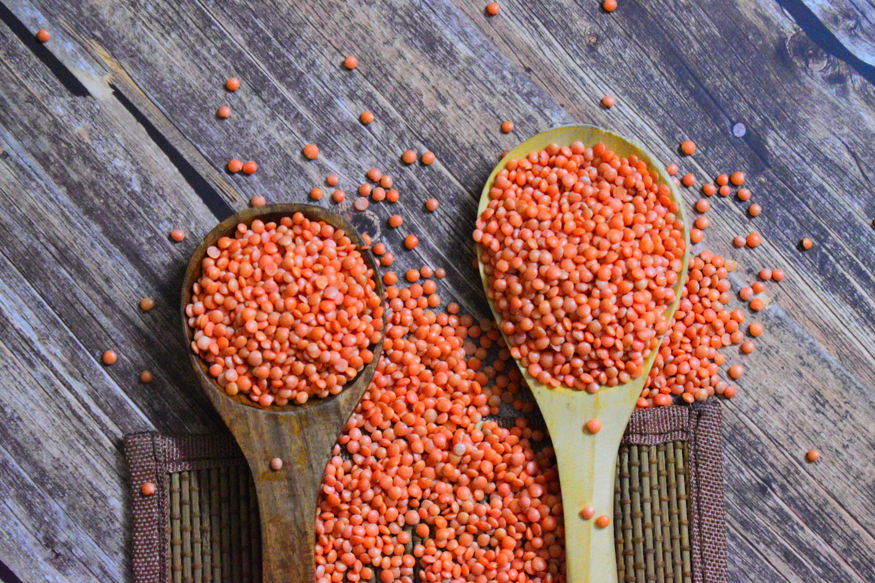 Two wooden spoons heaped with dry split red lentils on weathered boards