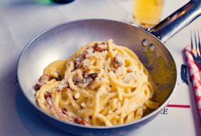 Spaghetti carbonara served in a metal pan with cheese.
