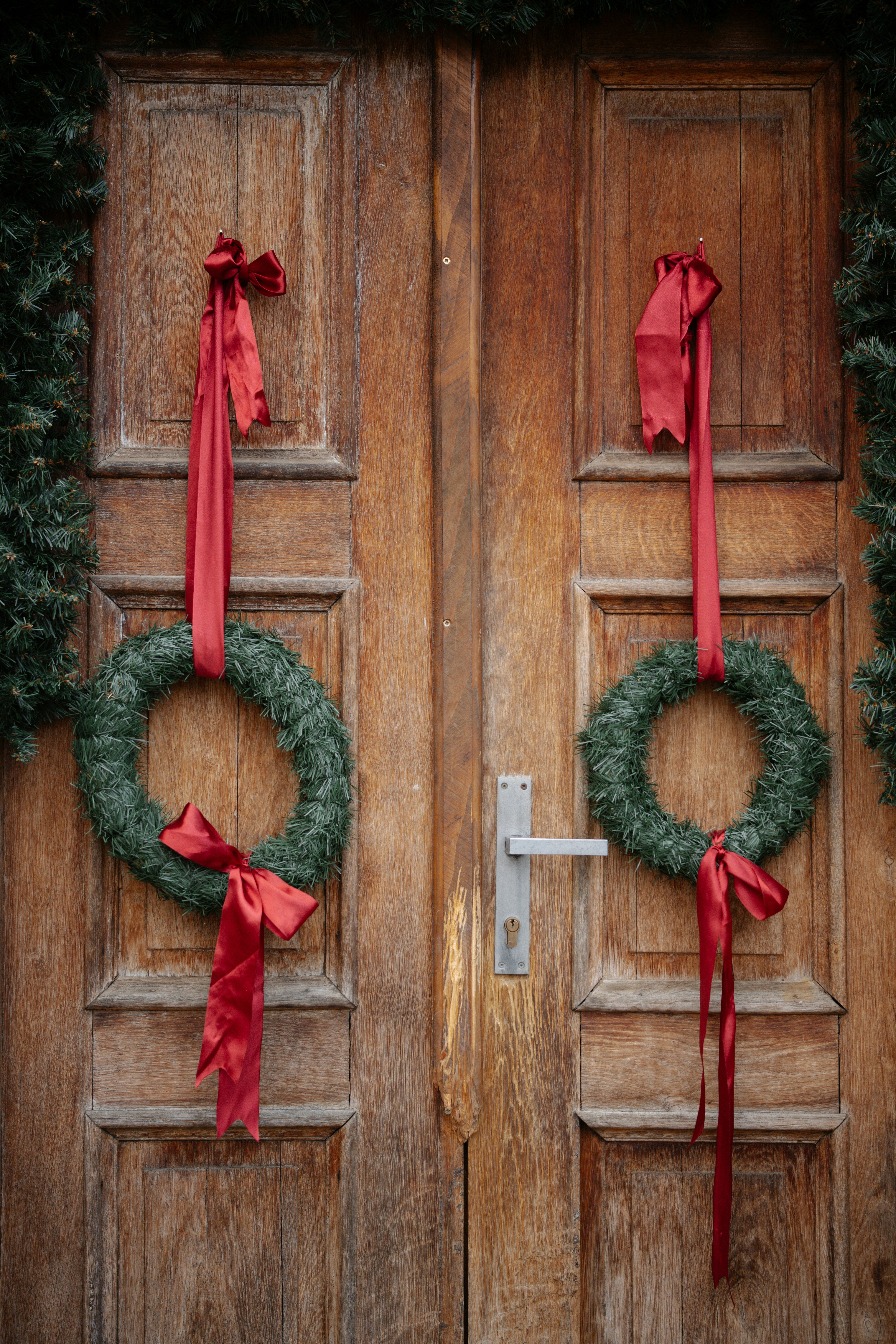 Two christmas wreaths hang on a wooden door.