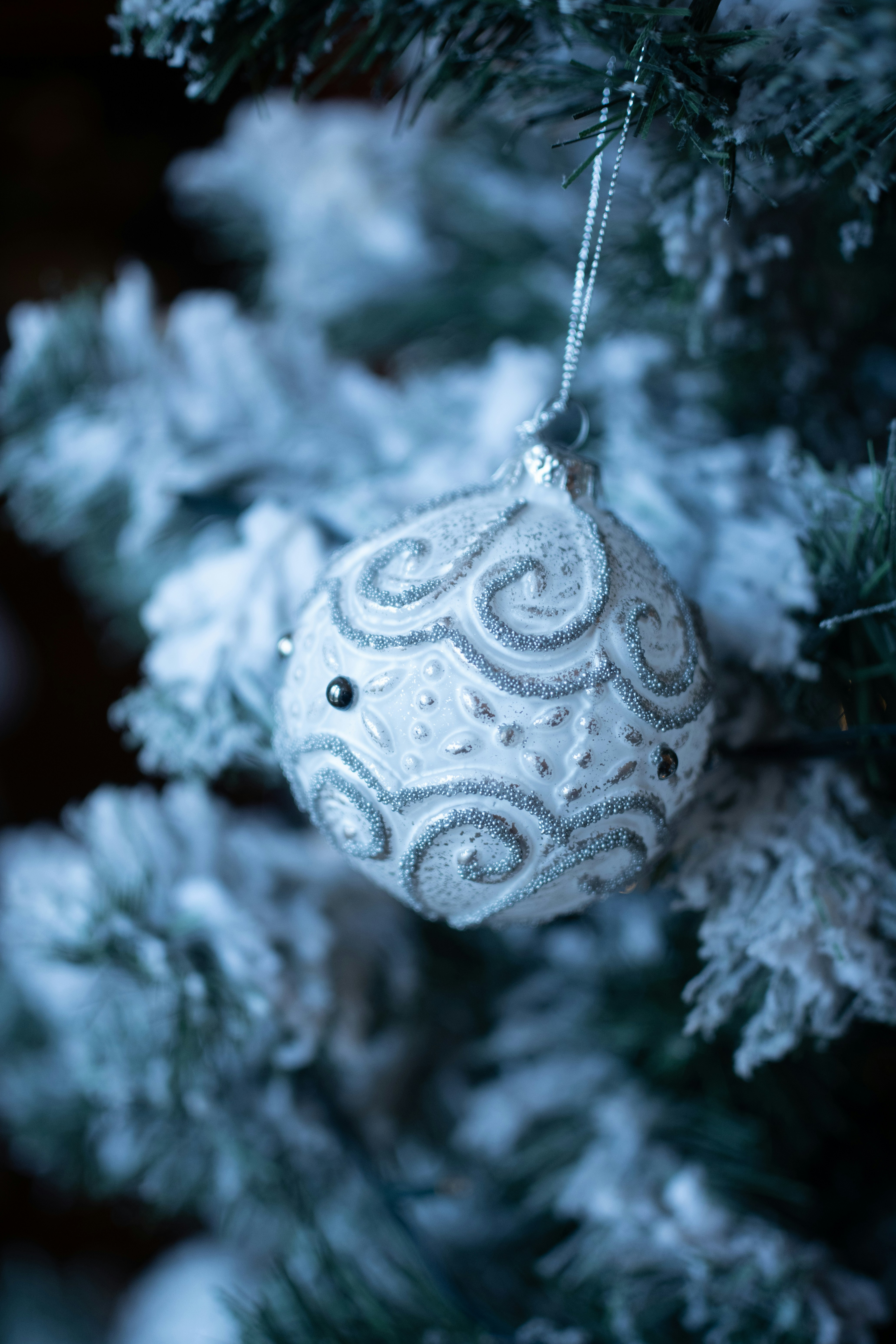 Ein weißer Weihnachtsanhänger hängt an einem schneebedeckten Baum.