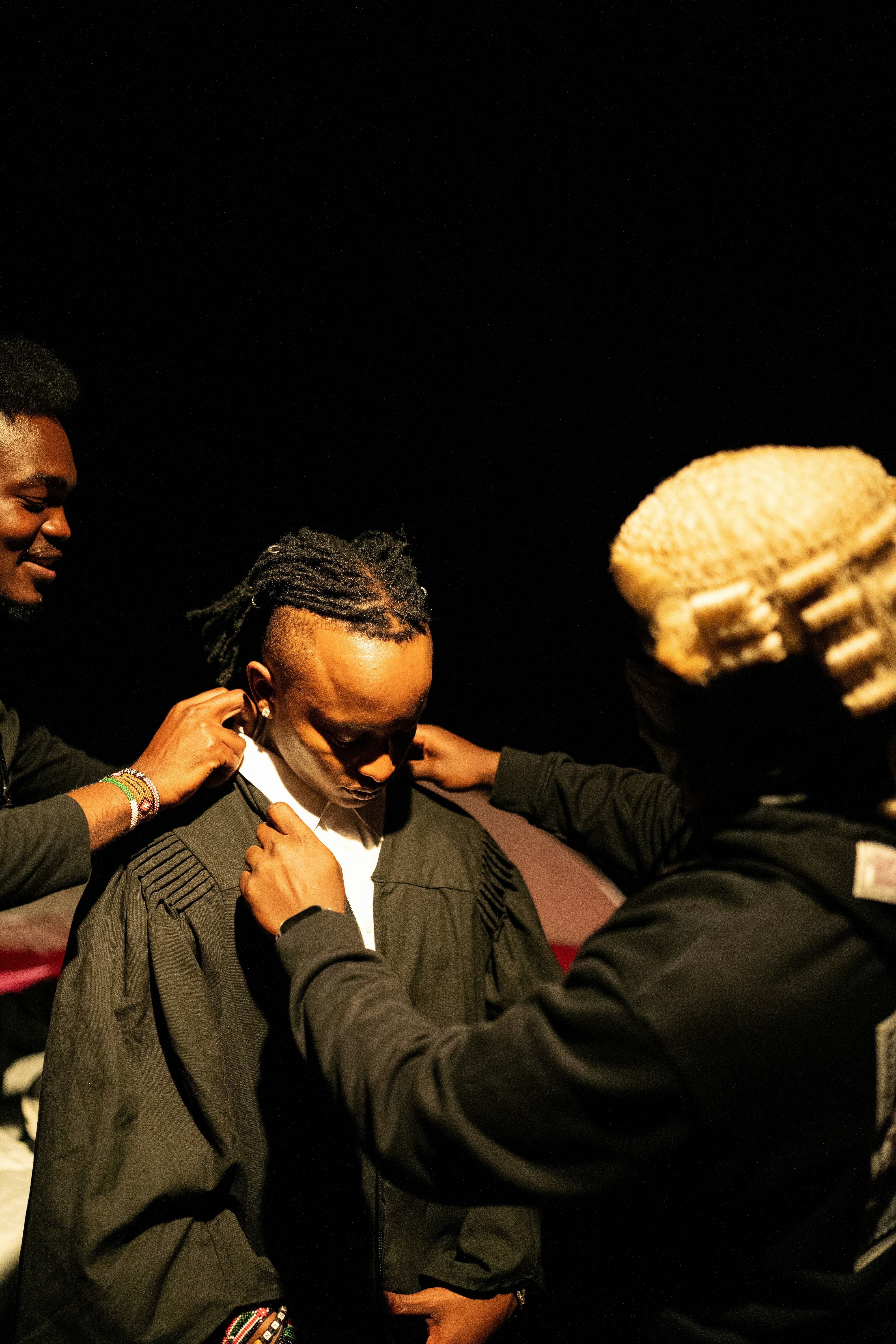 Three people in formal attire with one wearing a wig.