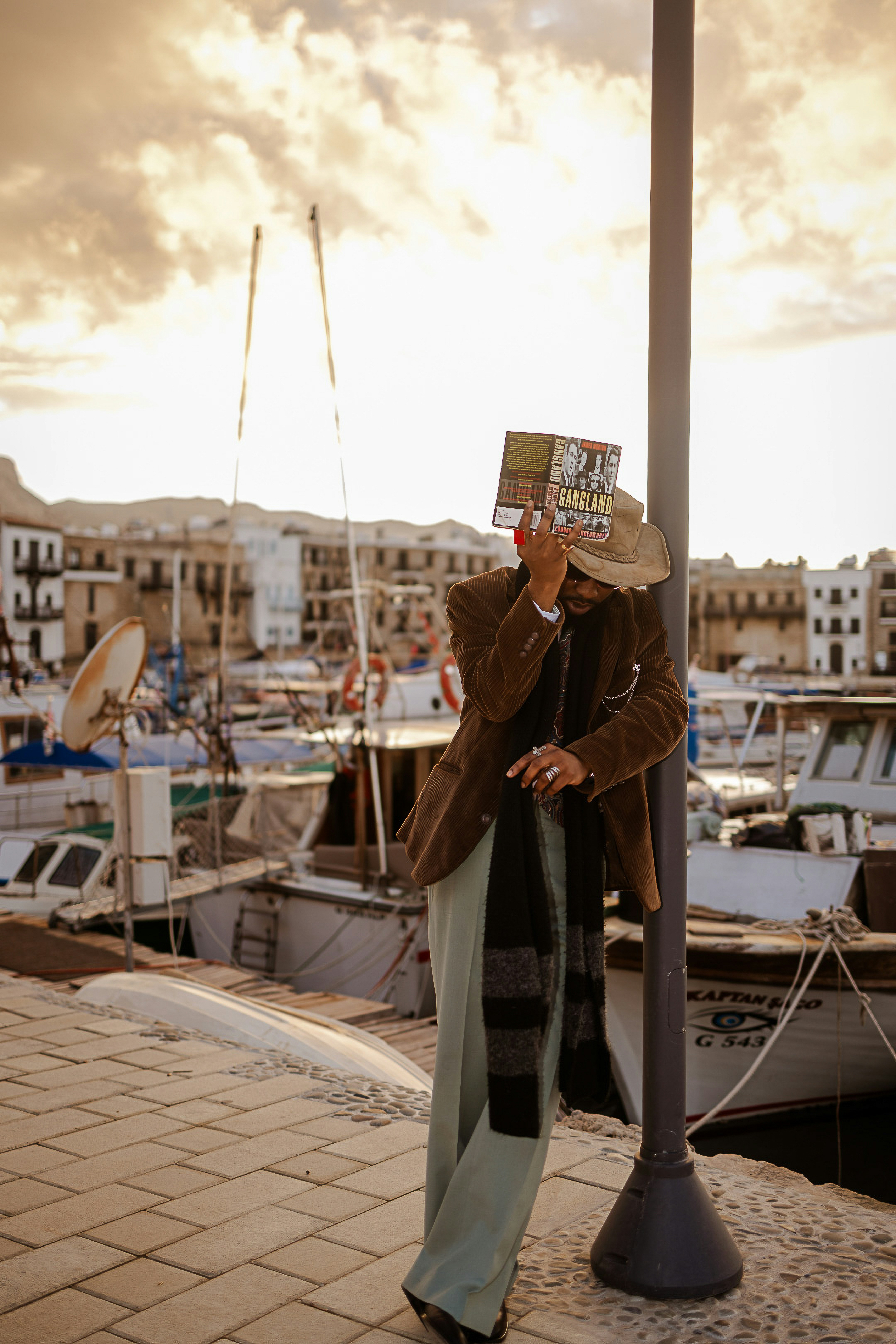Man in hat holding map obscuring face by harbor.