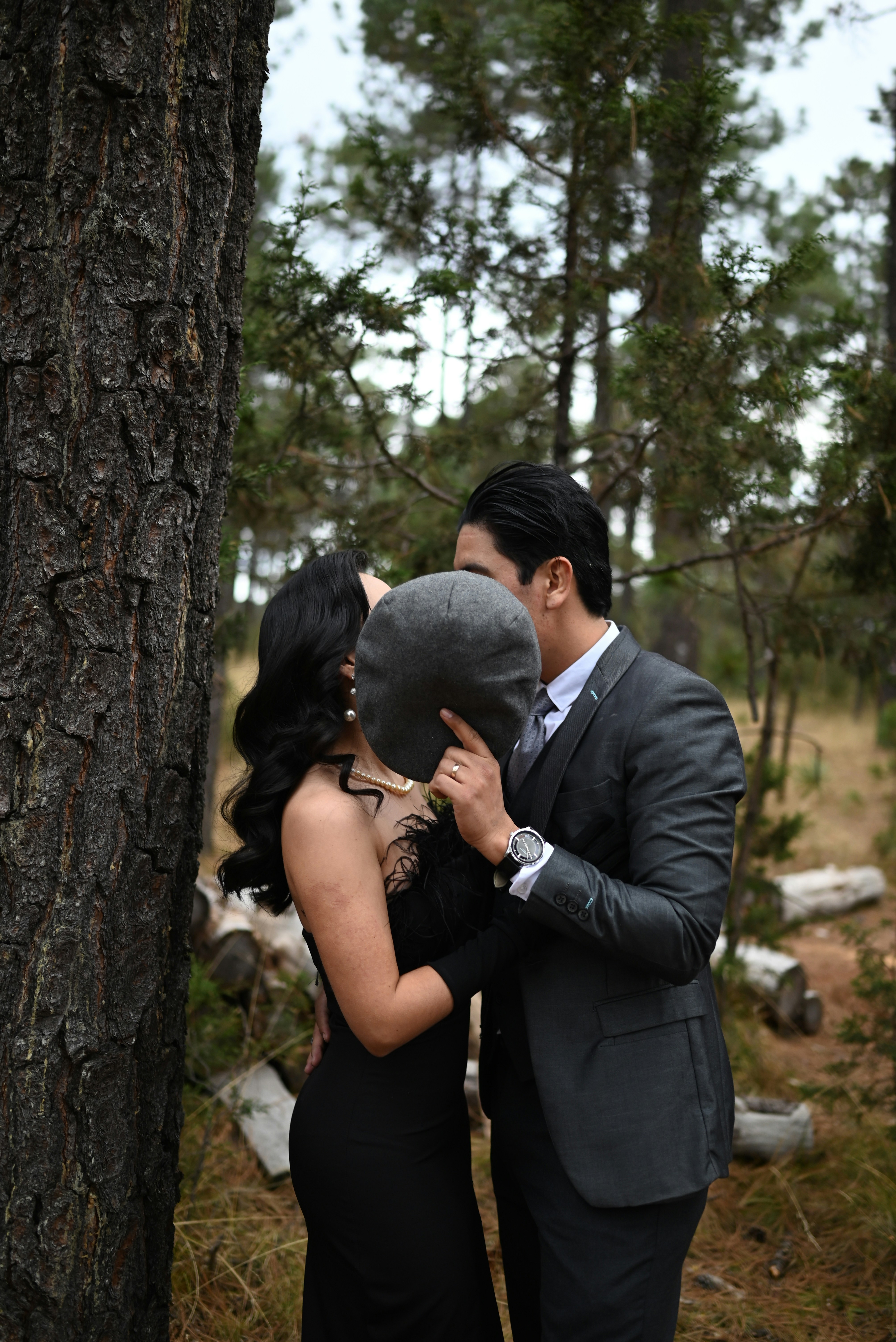Couple kissing behind a hat in a forest.
