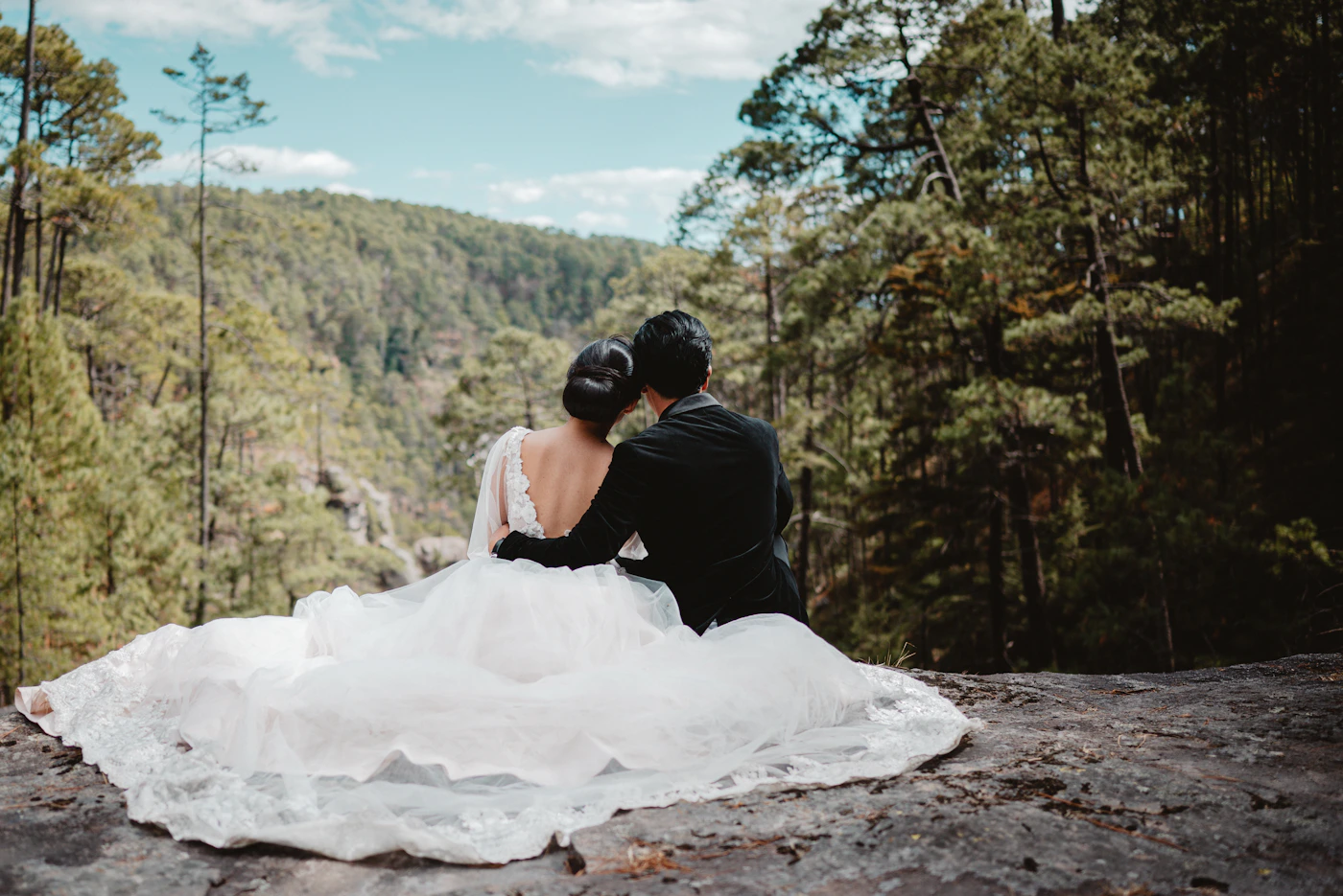 A couple in formal wedding attire sitting together on dramatic rocky terrain during their destination wedding elopement with an expansive wild landscape stretching below and around them