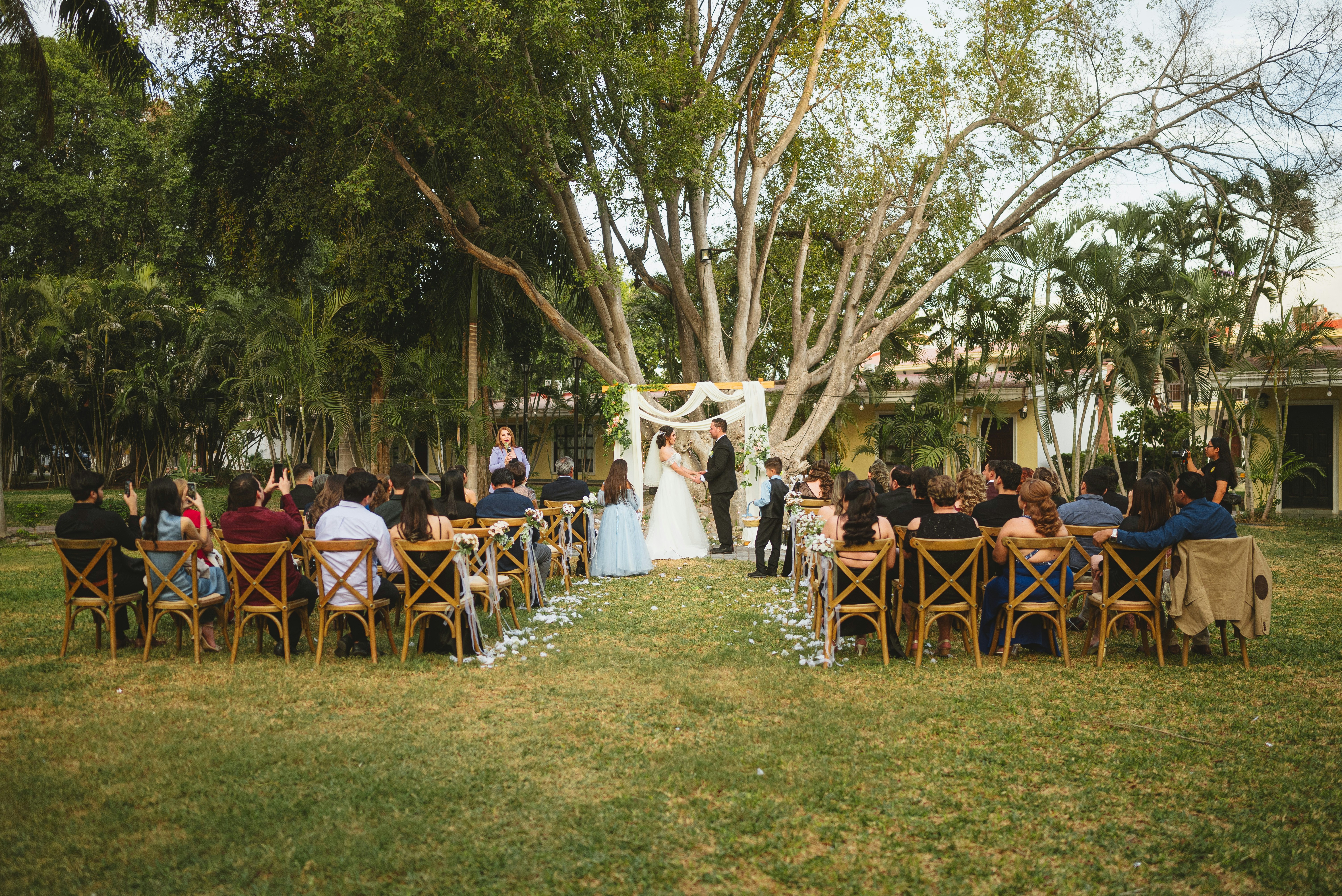 누에바파밀리아 - A wedding ceremony with guests seated on wooden chairs in a garden