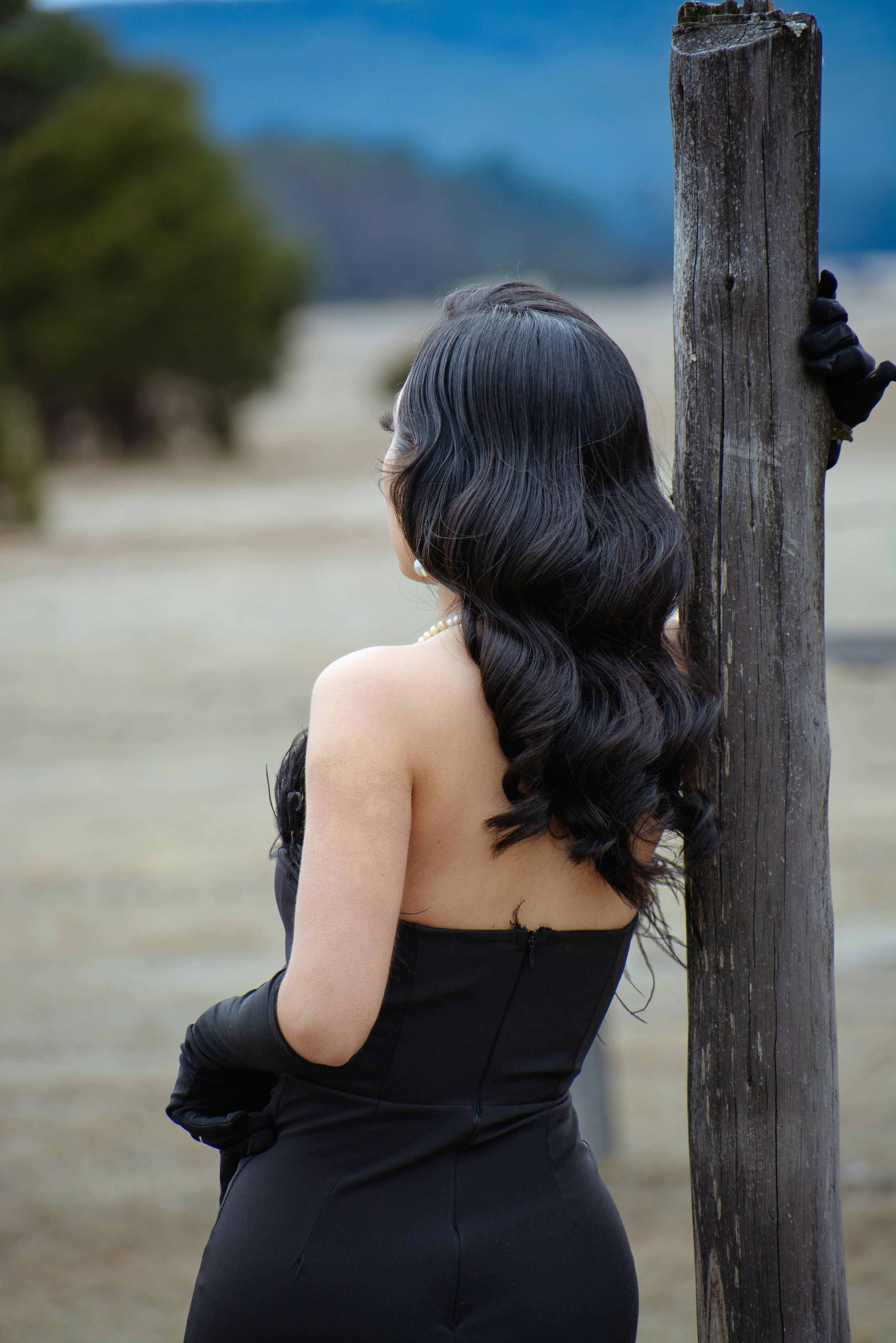 Woman in black dress leans on wooden post outdoors