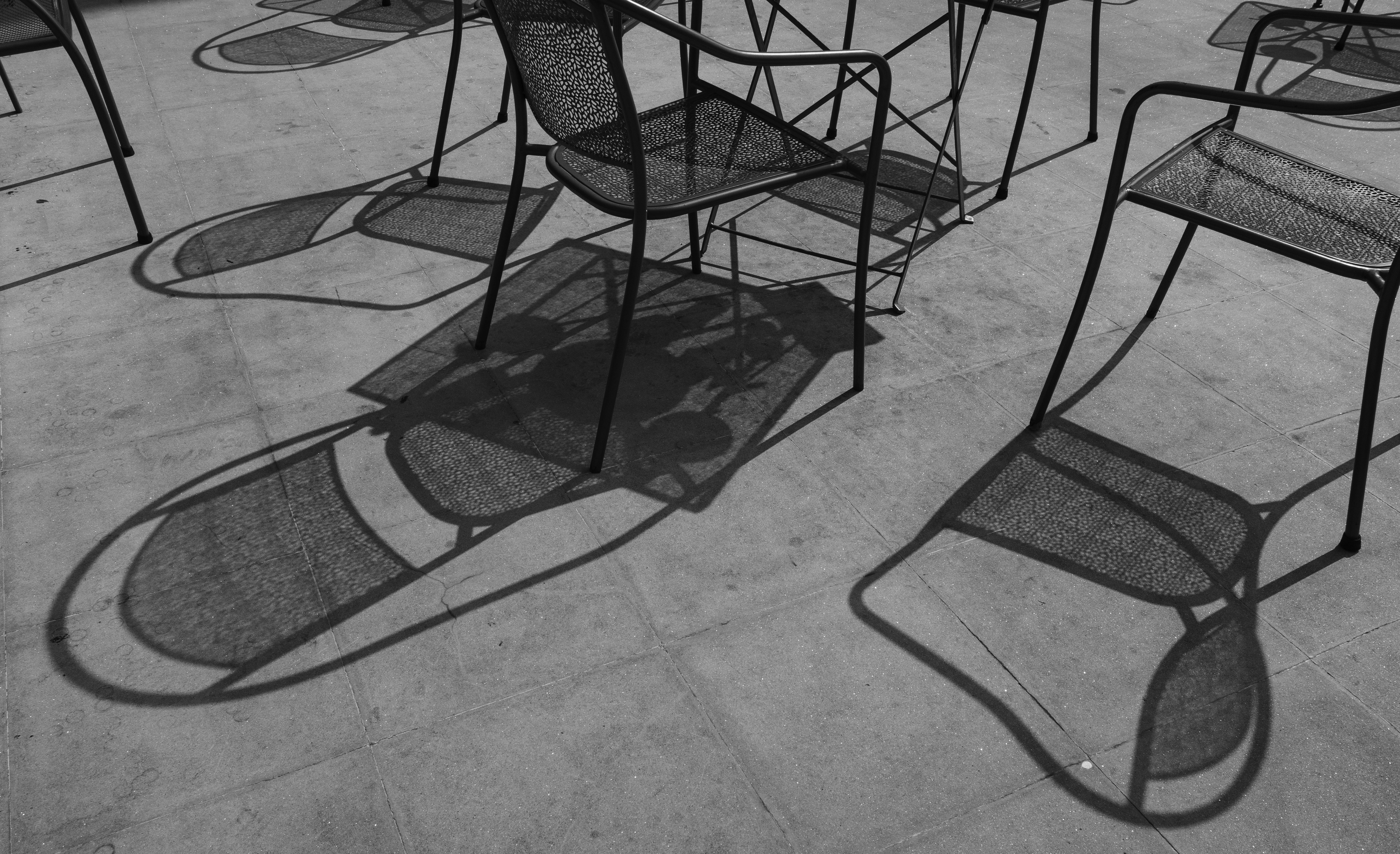 Metal chairs casting long shadows on concrete patio