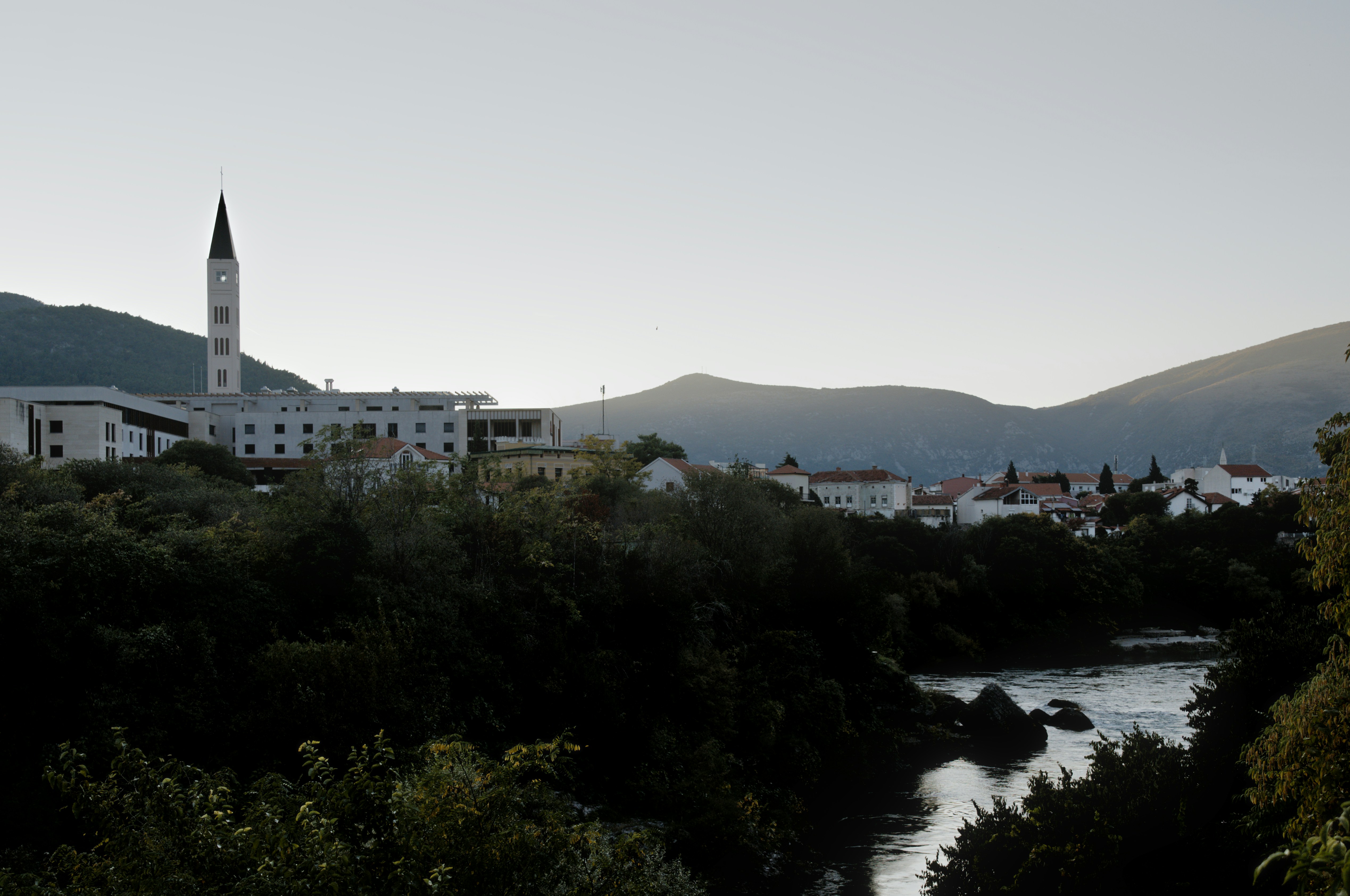 Town with a tall spire overlooks a river and hills.