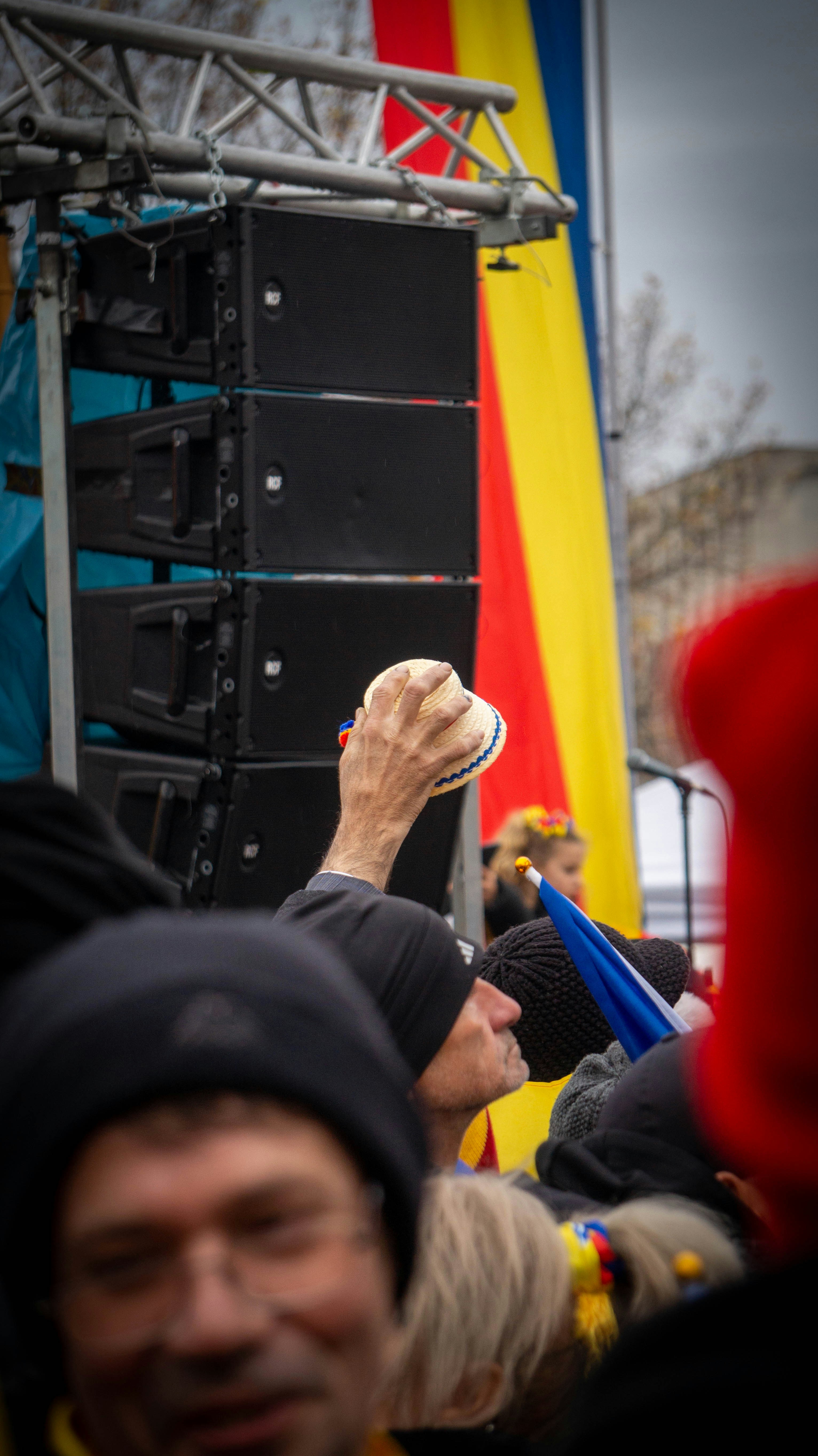 Man holding hat up at outdoor event with speakers