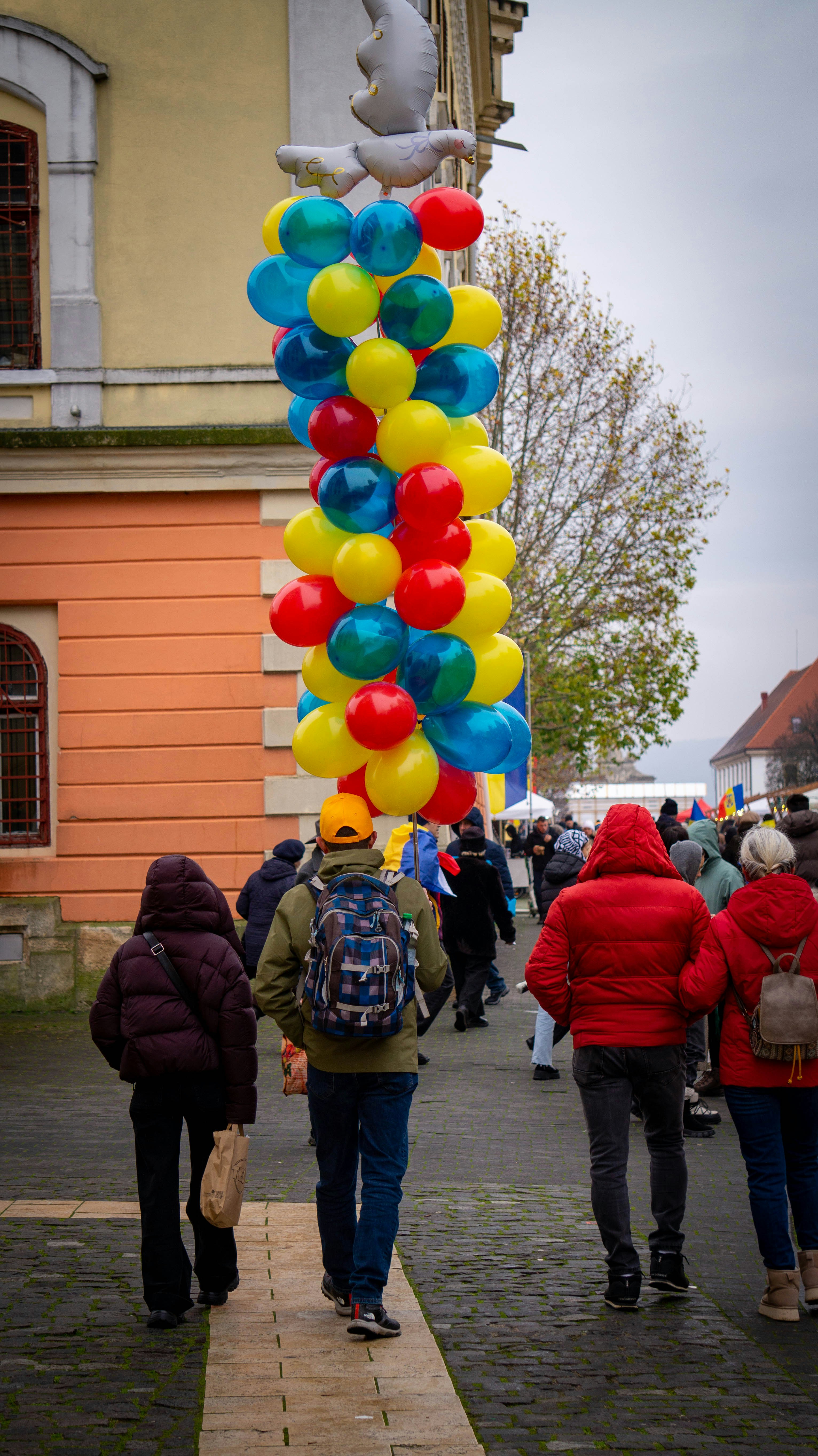 People walk past a tall column of colorful balloons.
