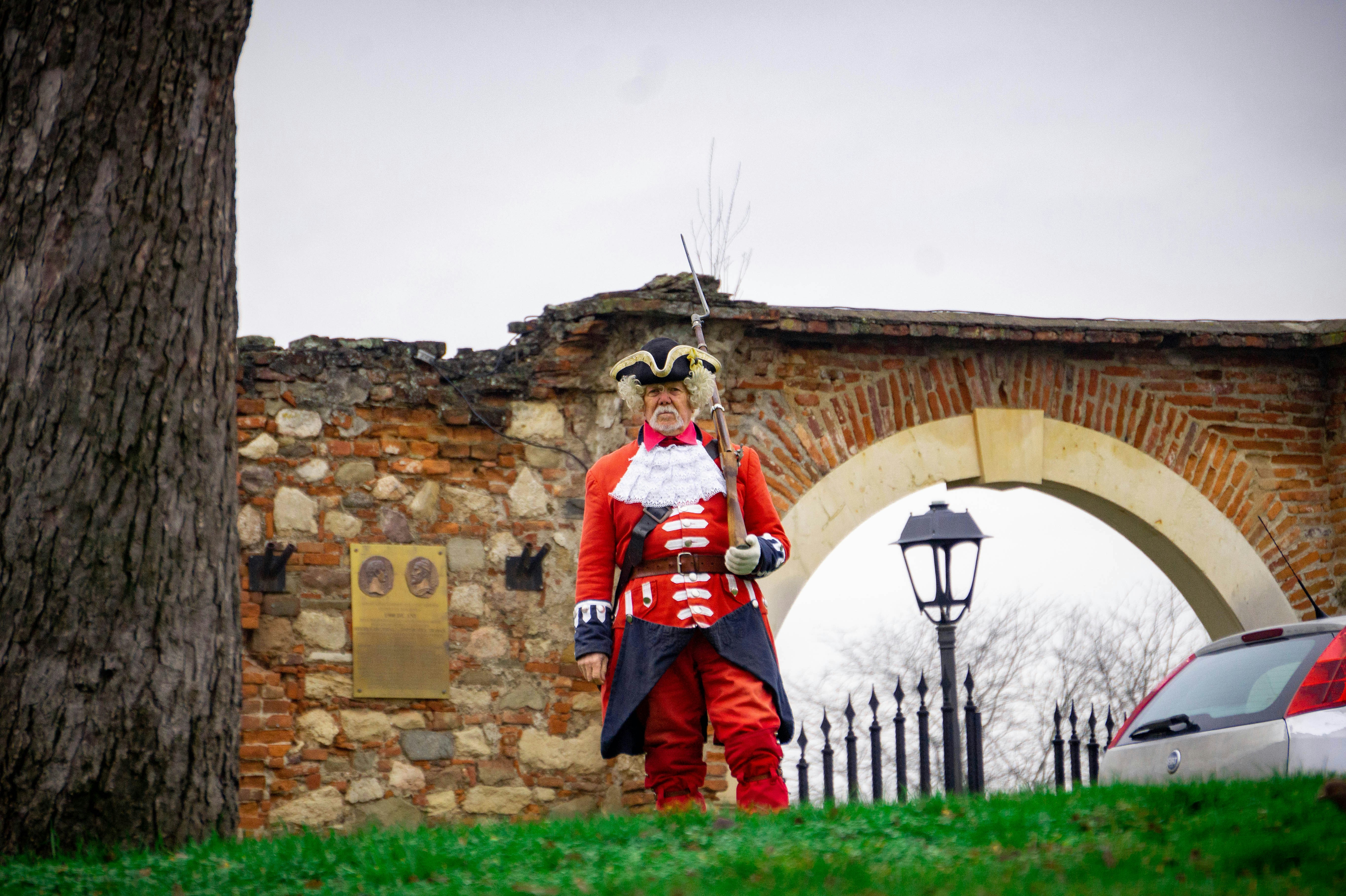 Man in historical red uniform standing near stone archway