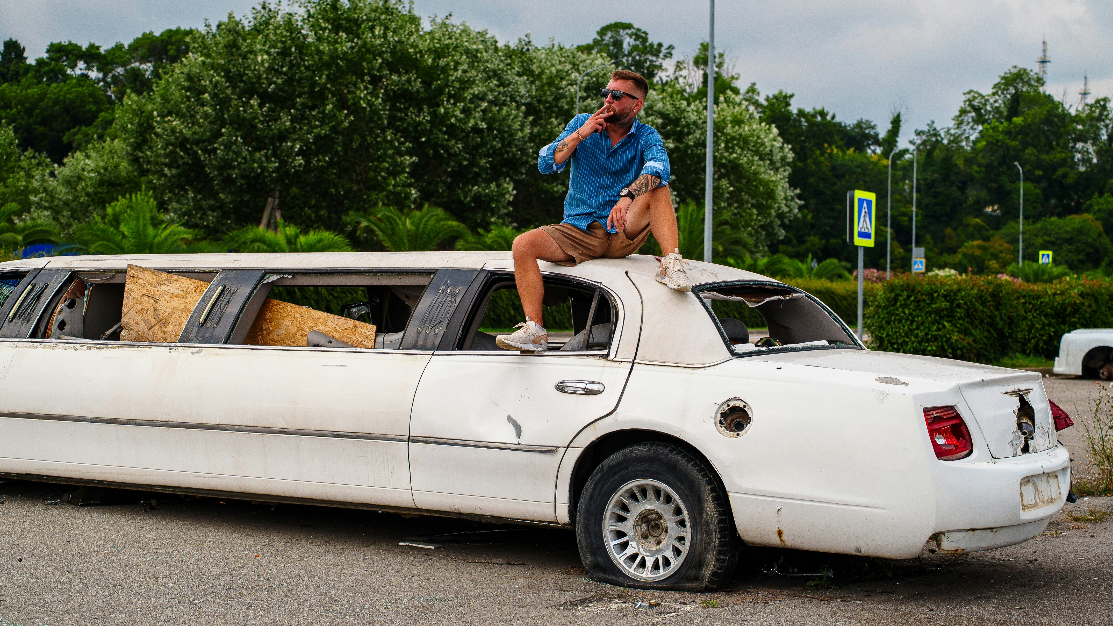 Man sits on top of damaged white limousine