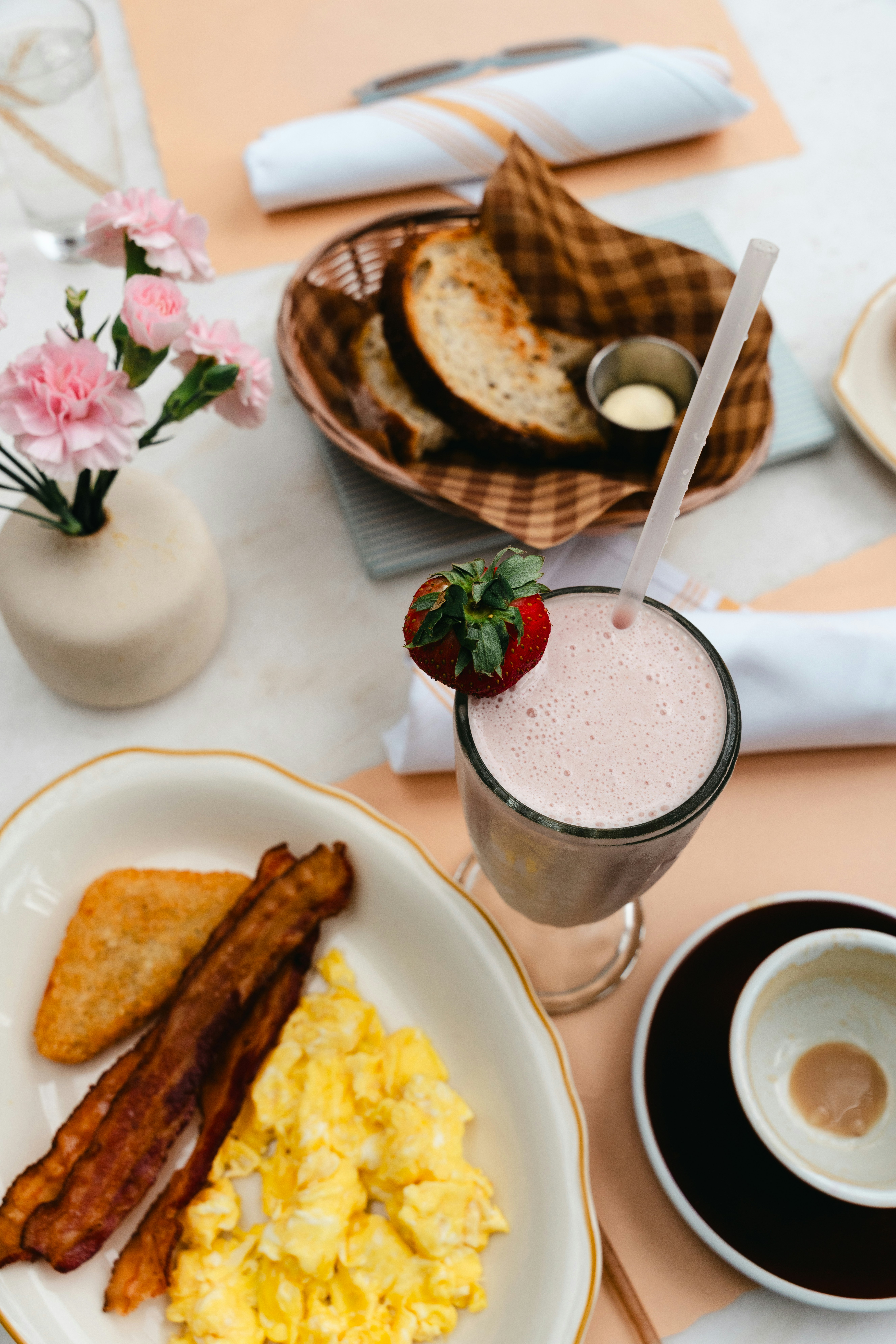Breakfast with scrambled eggs, bacon, hash brown, and milkshake.