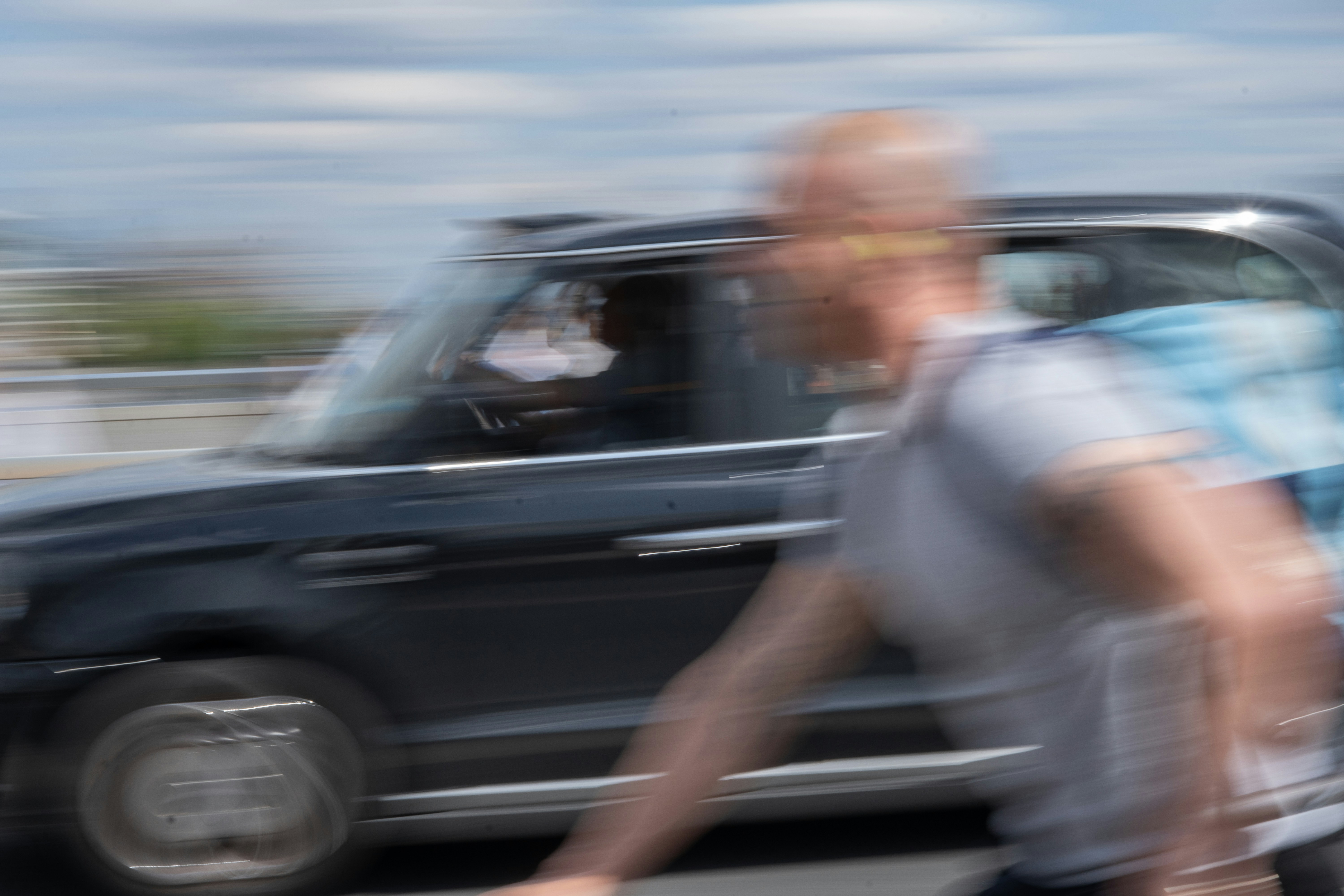 Man cycling past a black car on a street