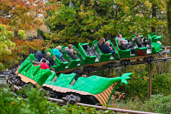 People riding a green dragon roller coaster through trees