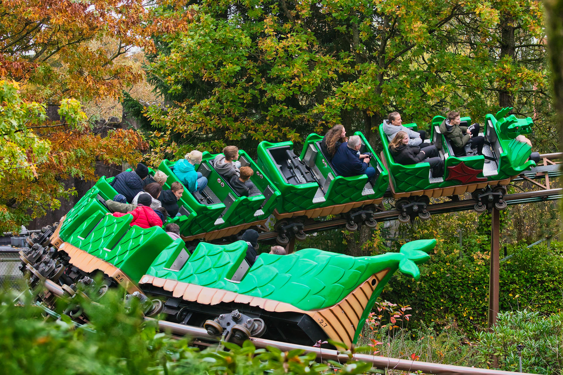 People riding a green dragon roller coaster through trees