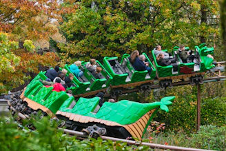 People riding a green dragon roller coaster through trees
