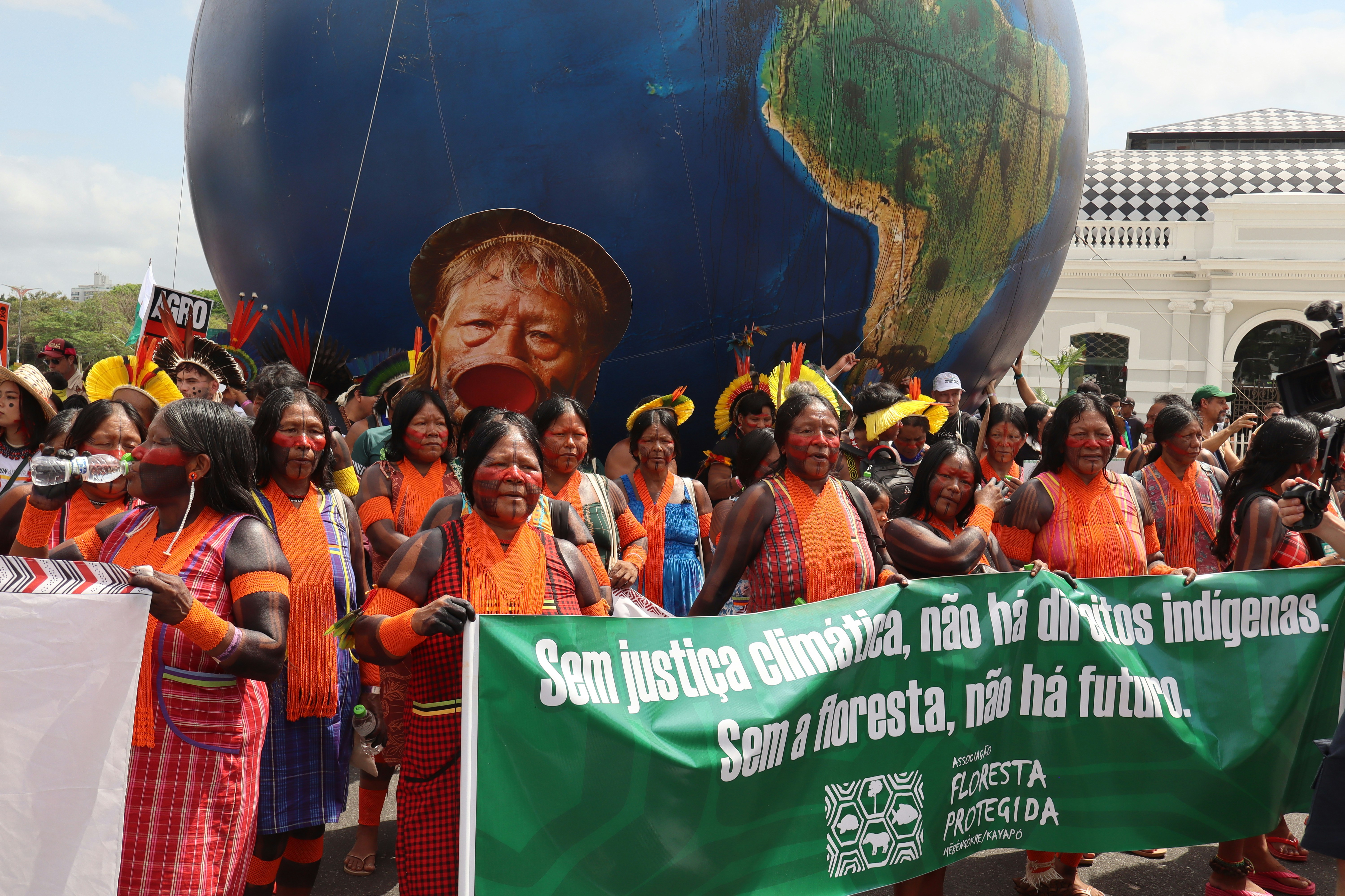 Indigenous people protest with a large globe behind them.