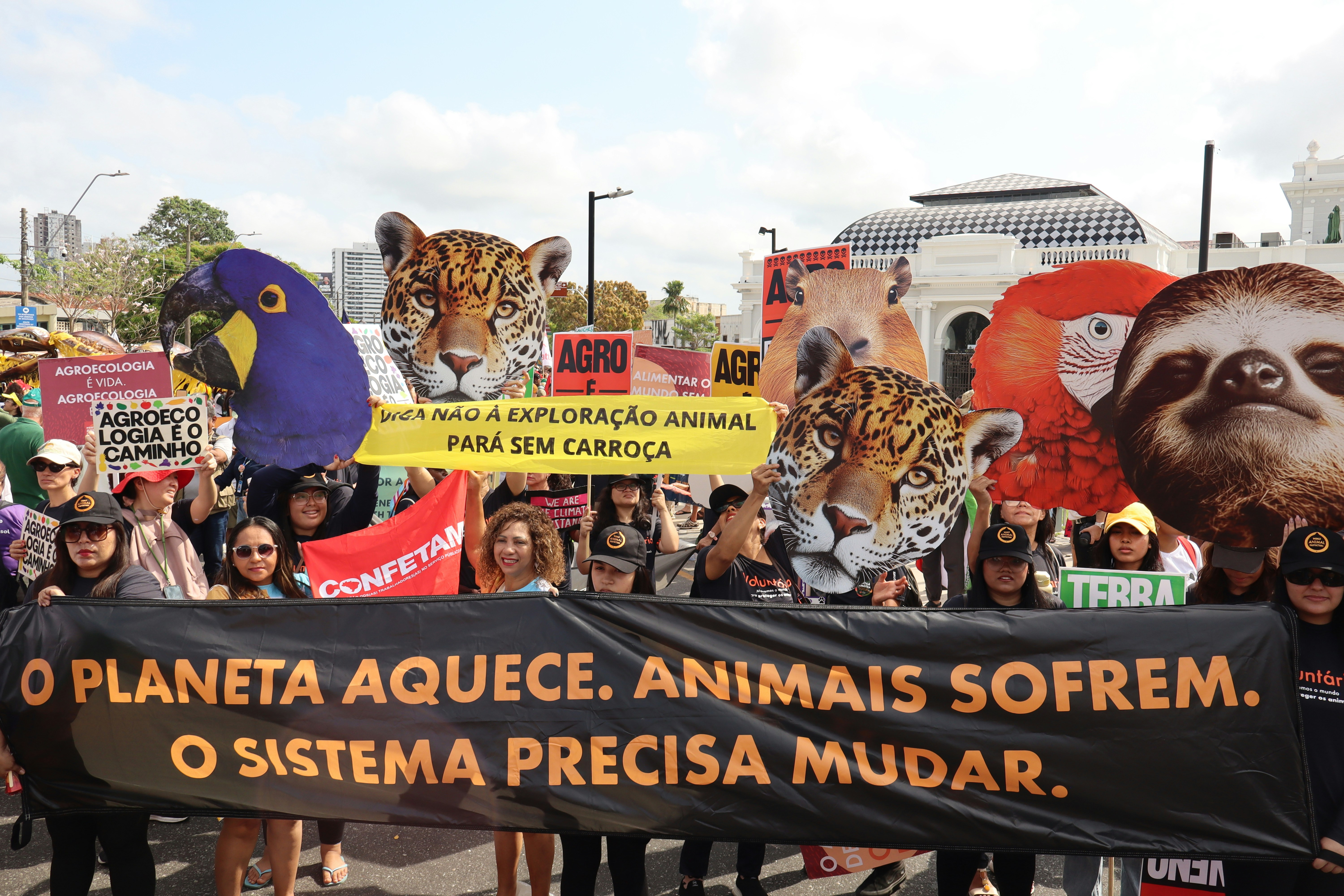 Protesters hold signs with animal faces and banners at banner.