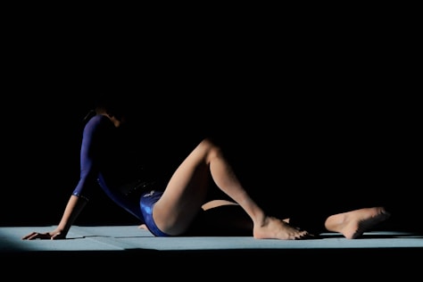 Gymnast in blue leotard on floor exercise mat.