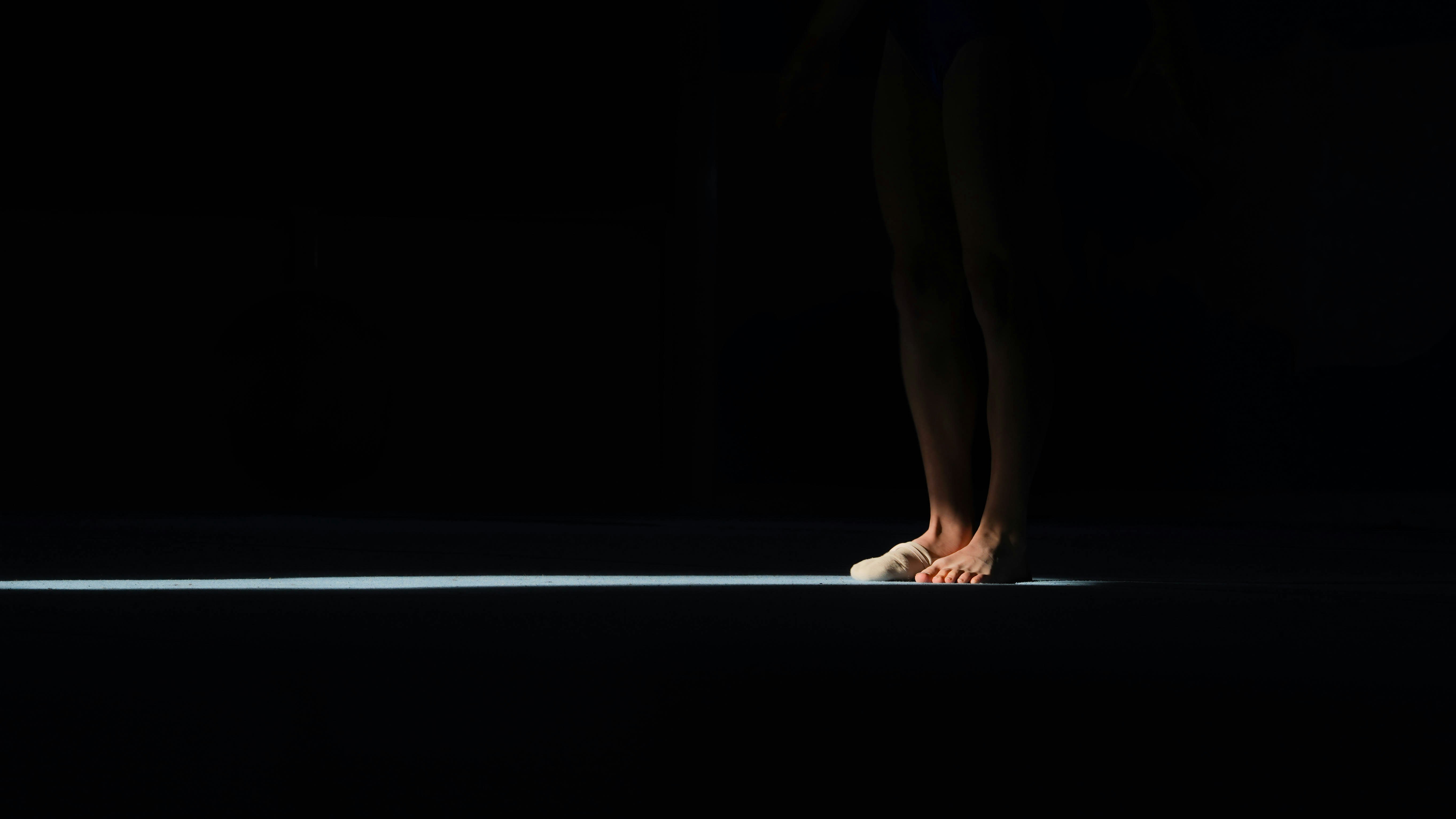 A person's bare feet illuminated by a single light beam.