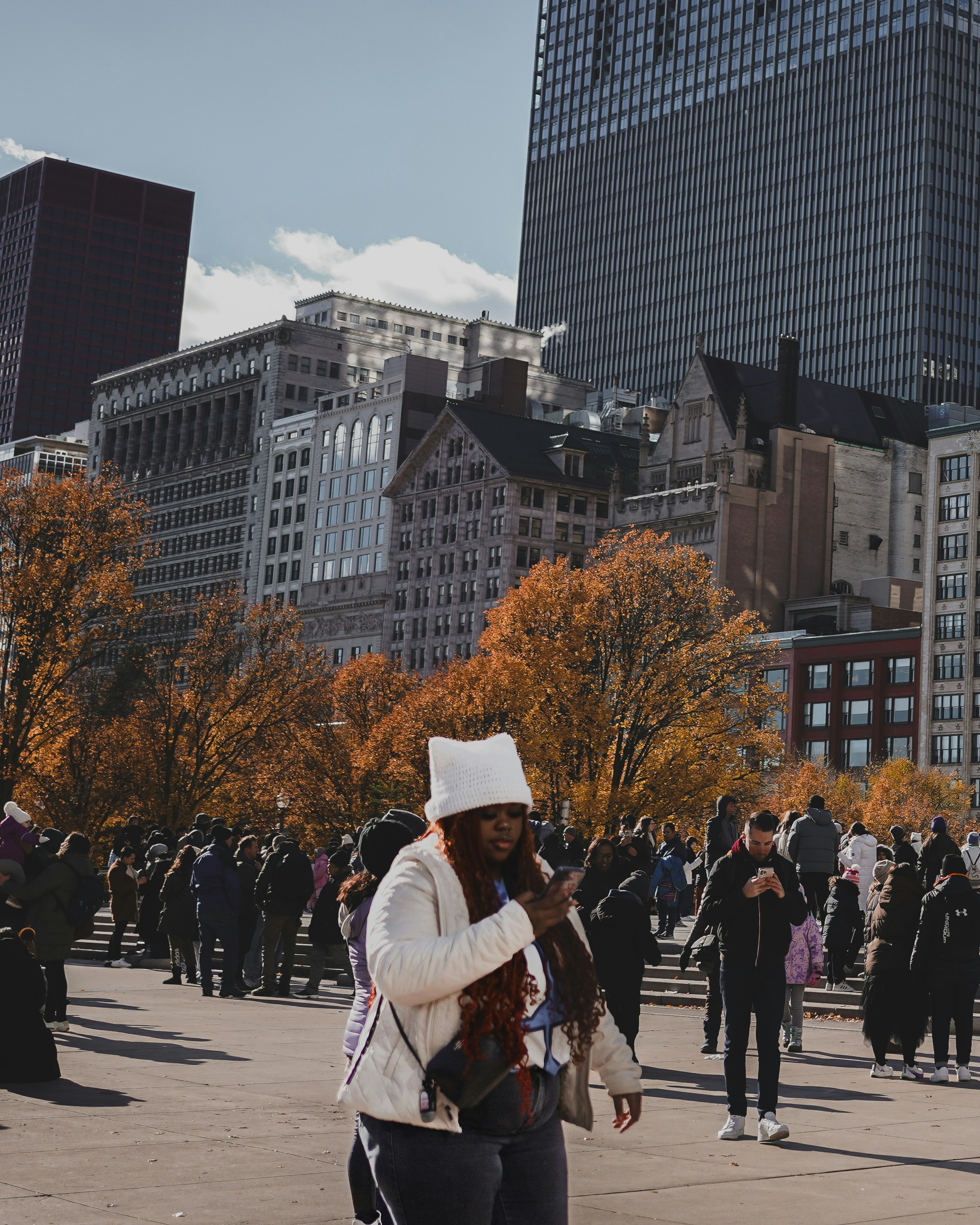 People gathered in a city park with autumn trees.