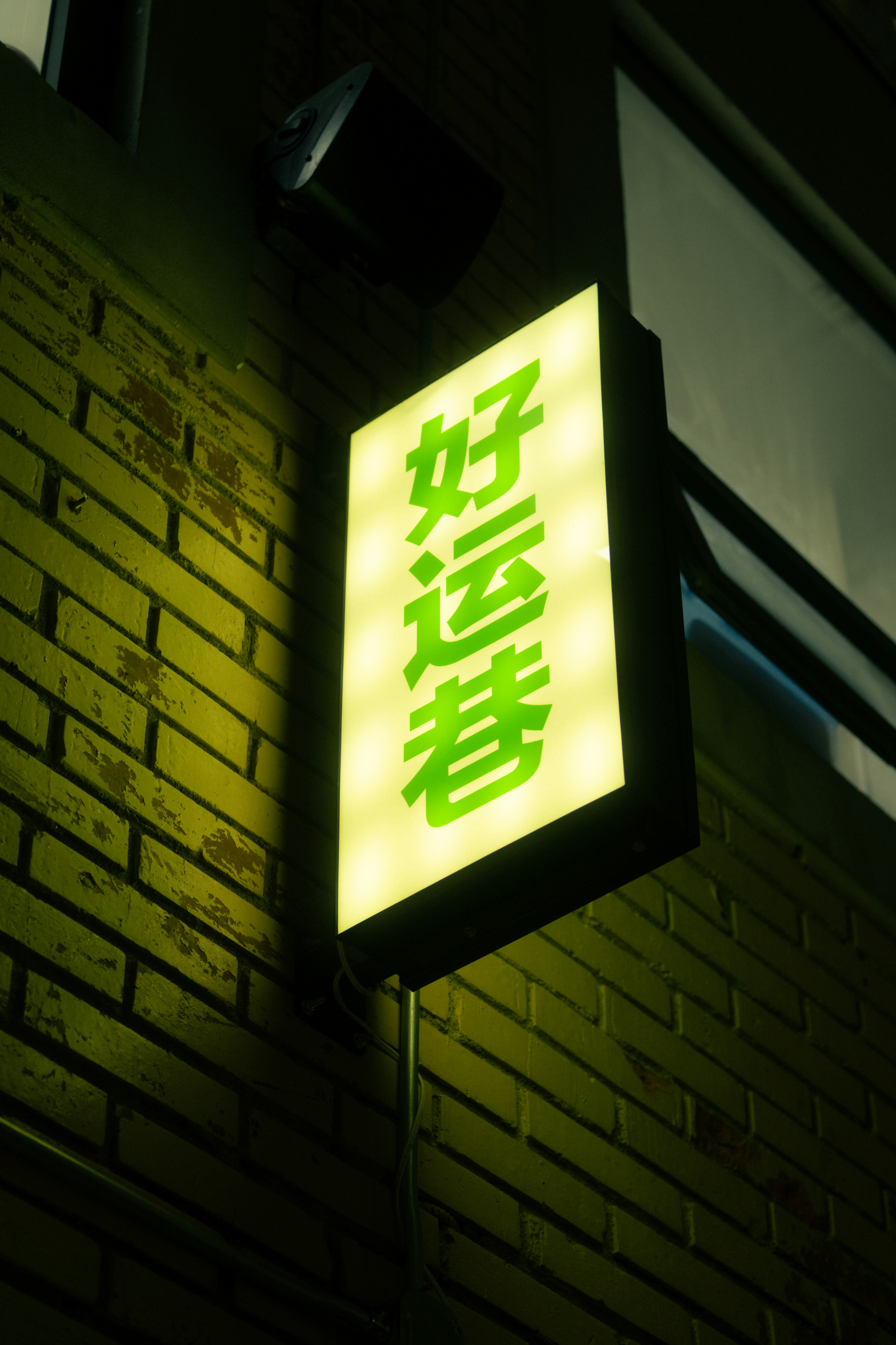Green neon sign with asian characters on brick wall.