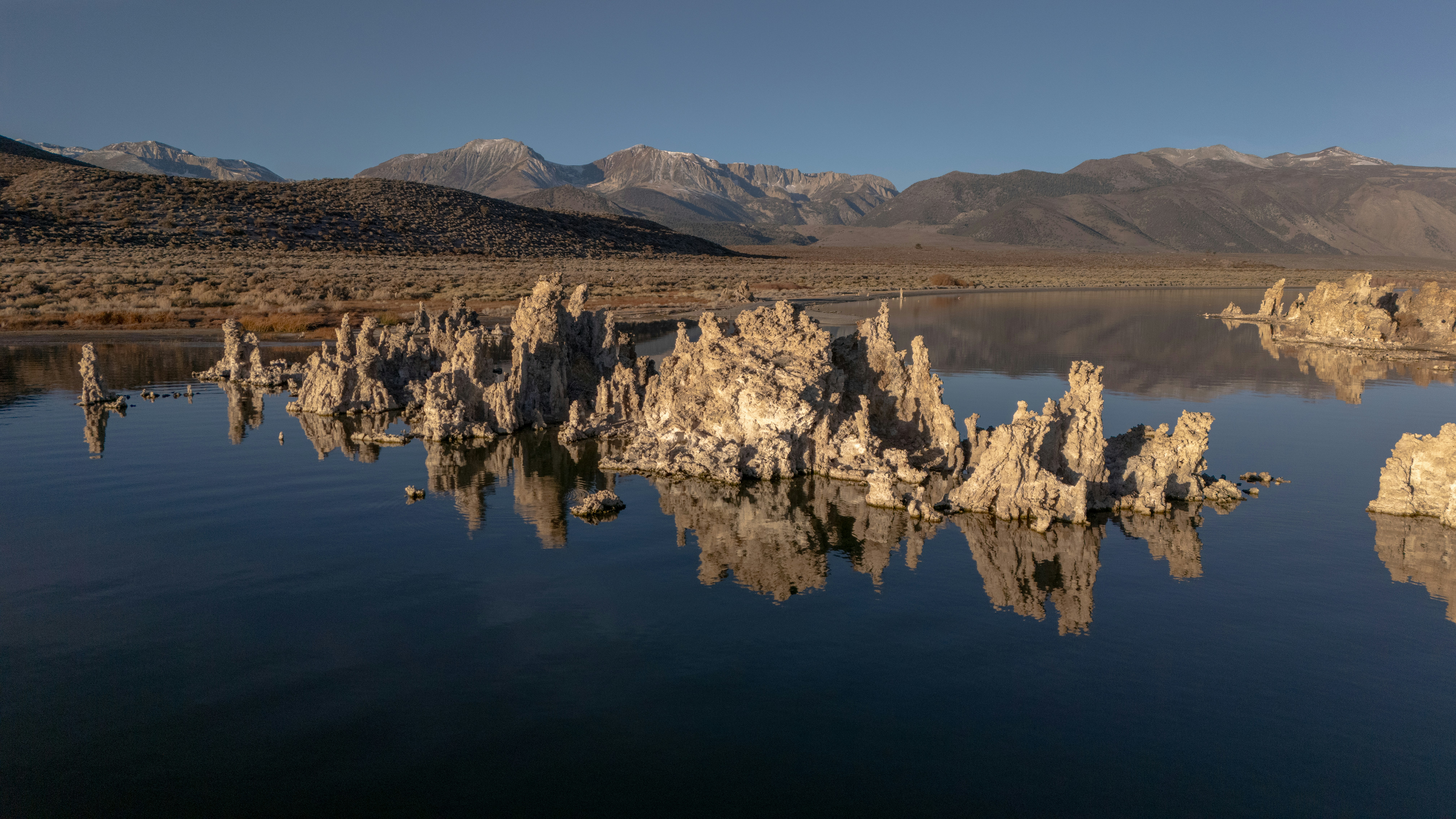 Torres de toba reflejadas en un lago tranquilo con montañas.