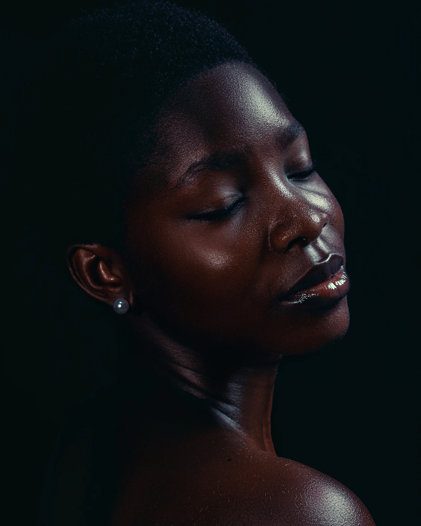 A woman with glowing skin and a pearl earring, eyes closed in soft light