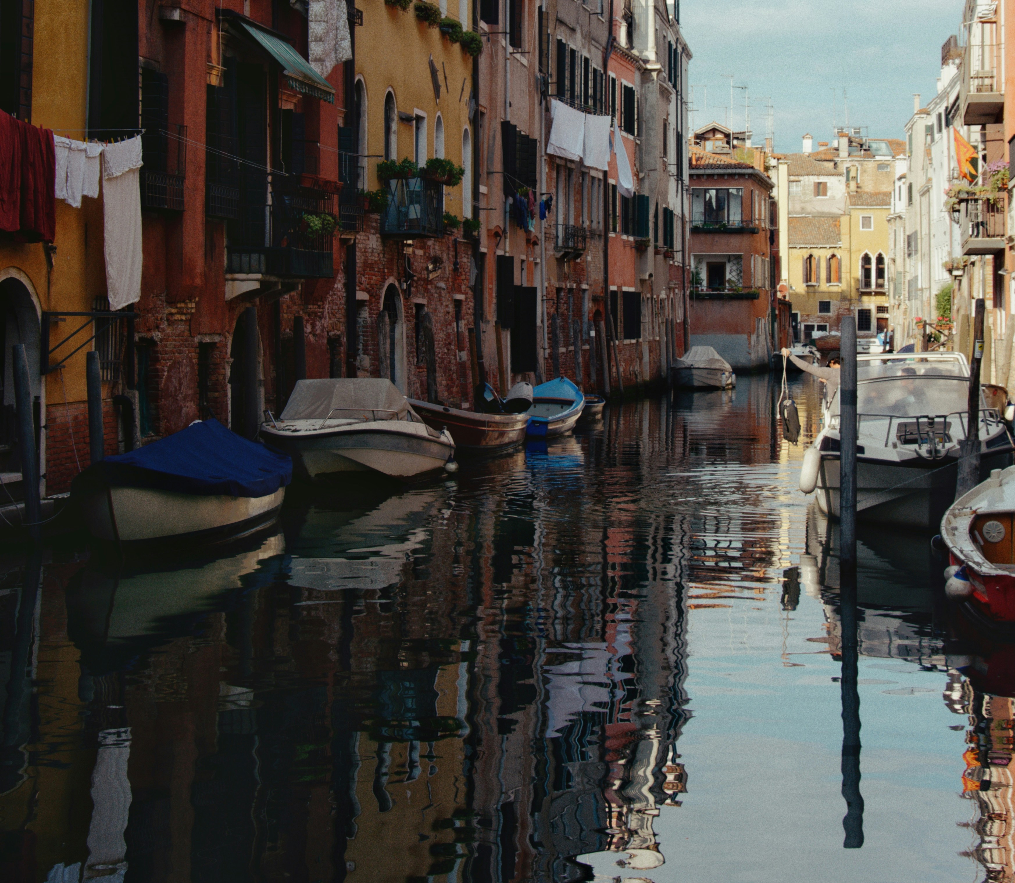 Boats docked in a narrow canal with buildings reflecting.