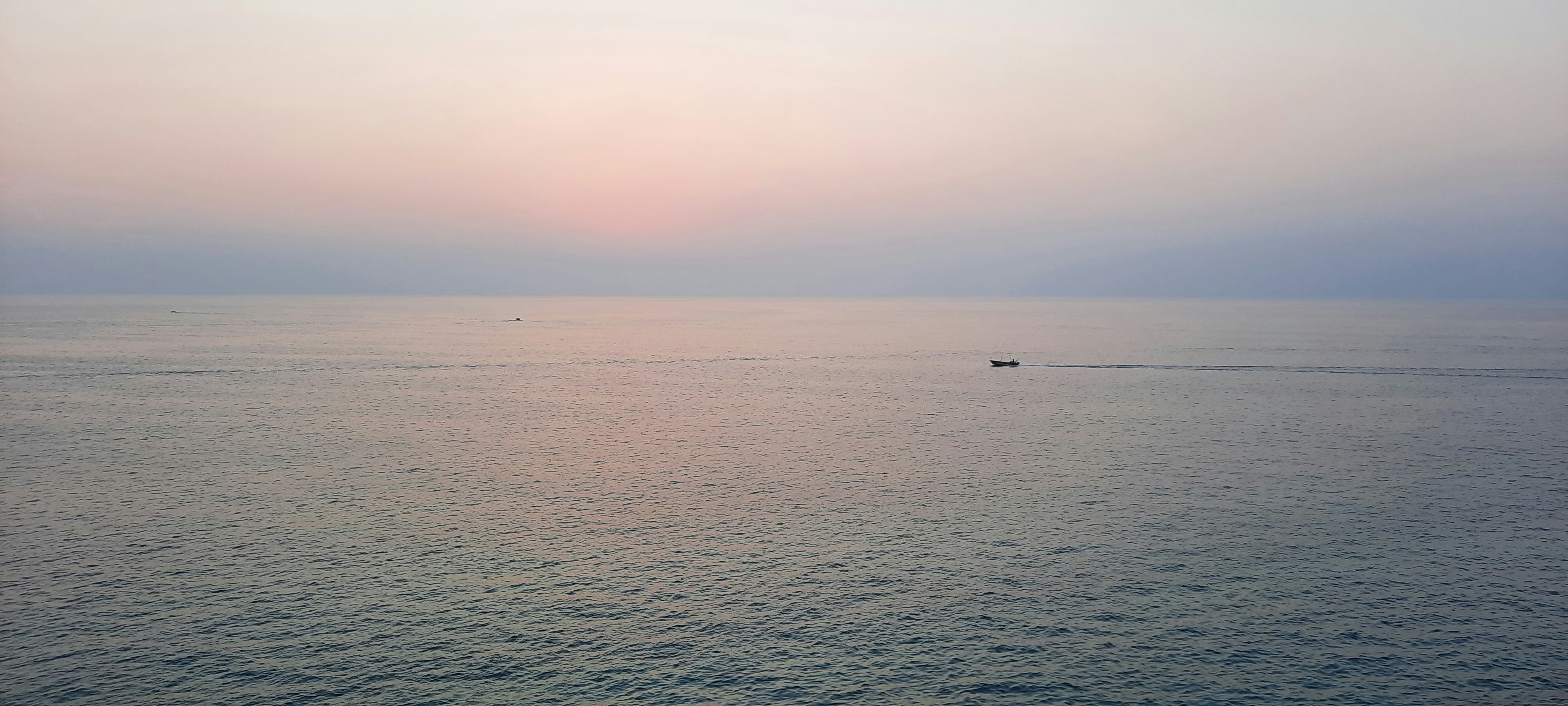 A small boat sails on the ocean at sunset.