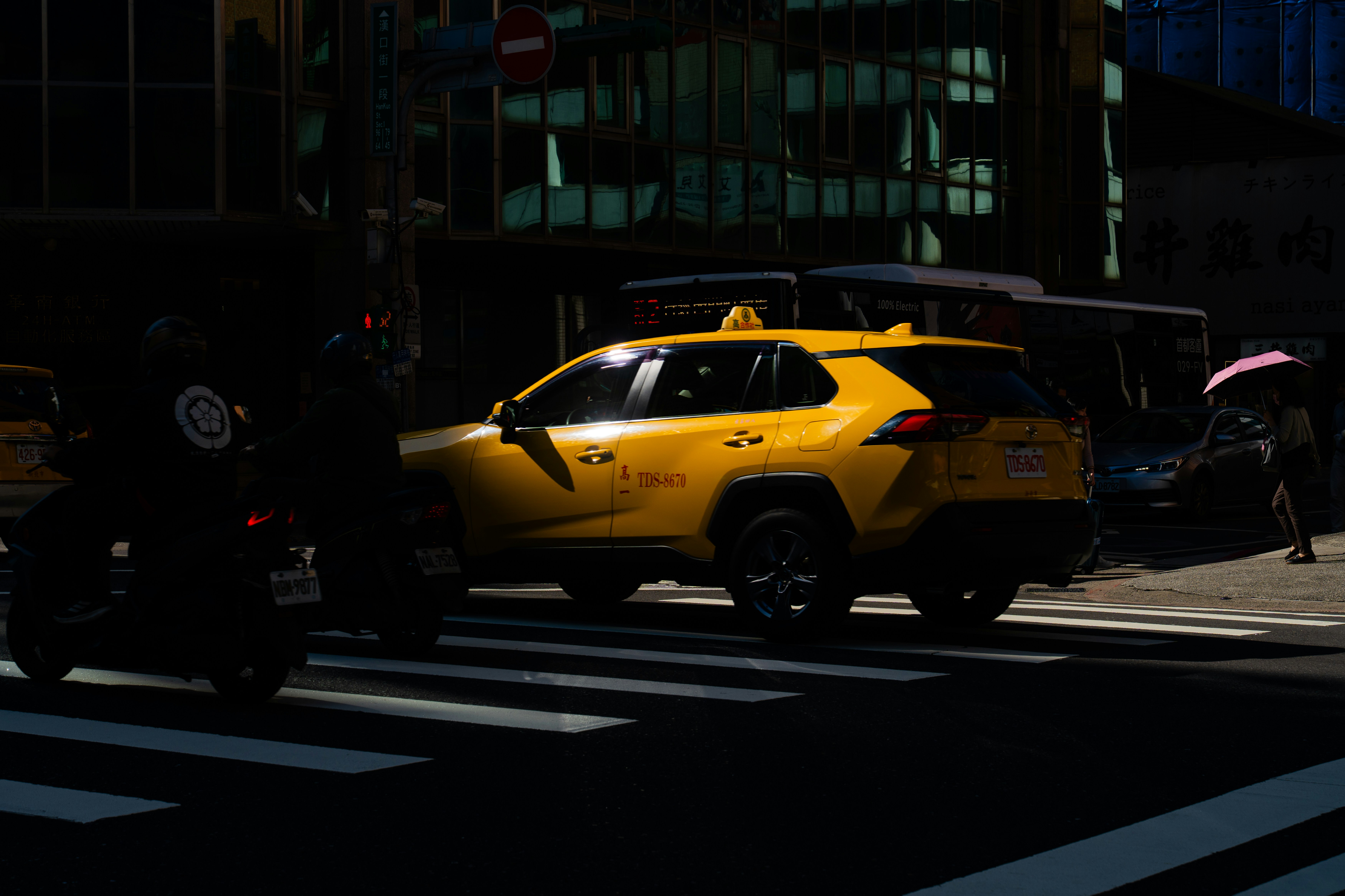 Yellow taxi driving on a city street at night.