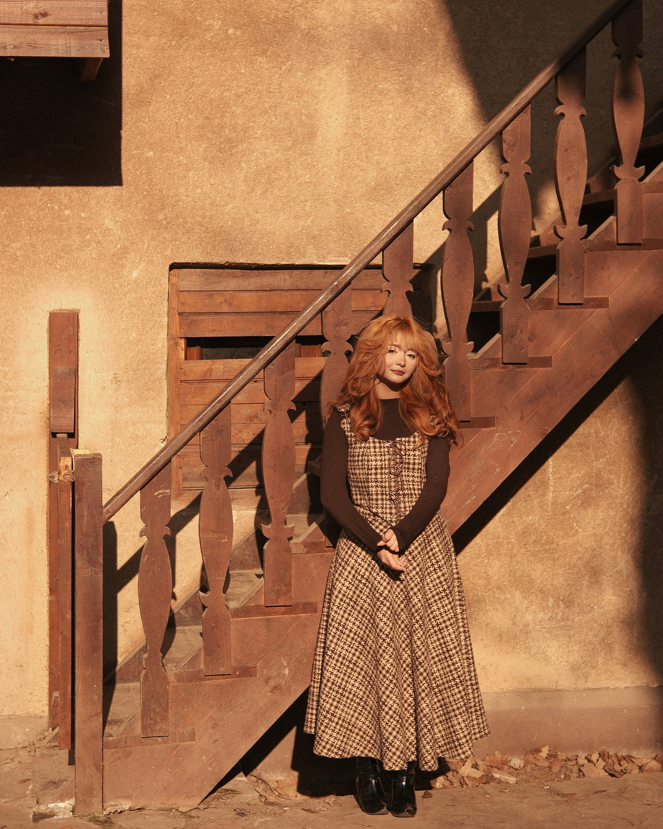 Woman in plaid dress standing by wooden stairs.