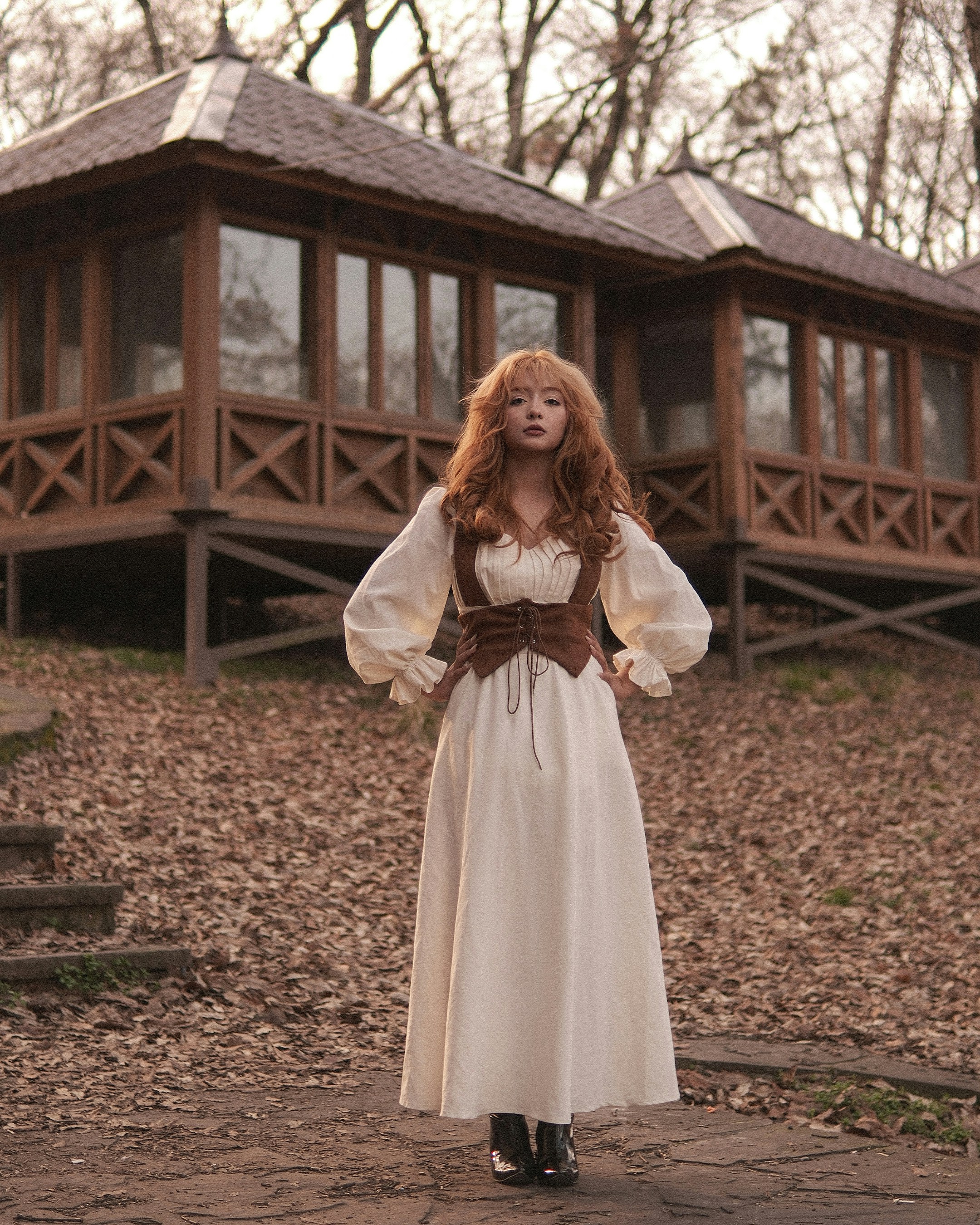 Woman in vintage dress stands outdoors near wooden gazebos