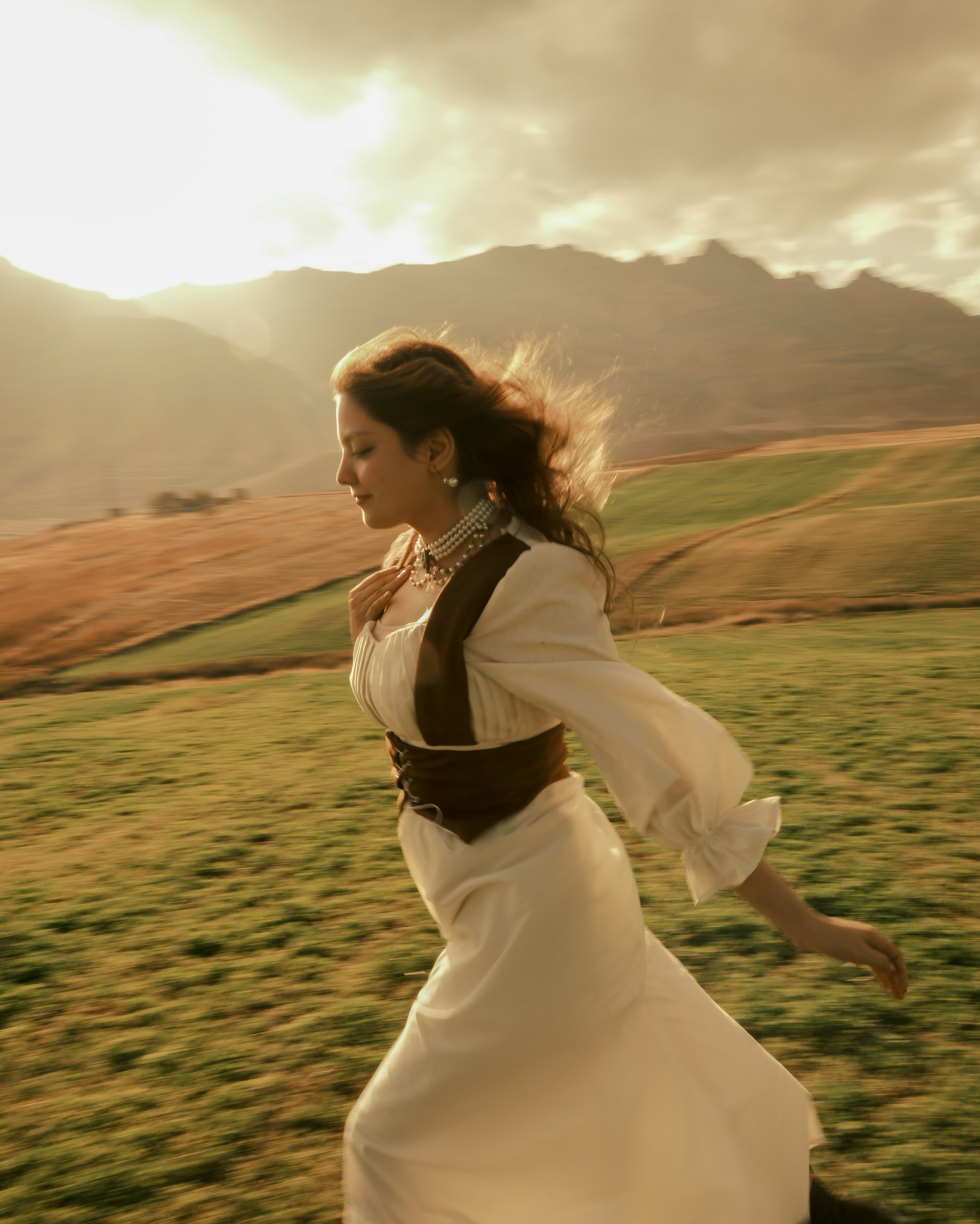 Woman in white dress running through a grassy field.